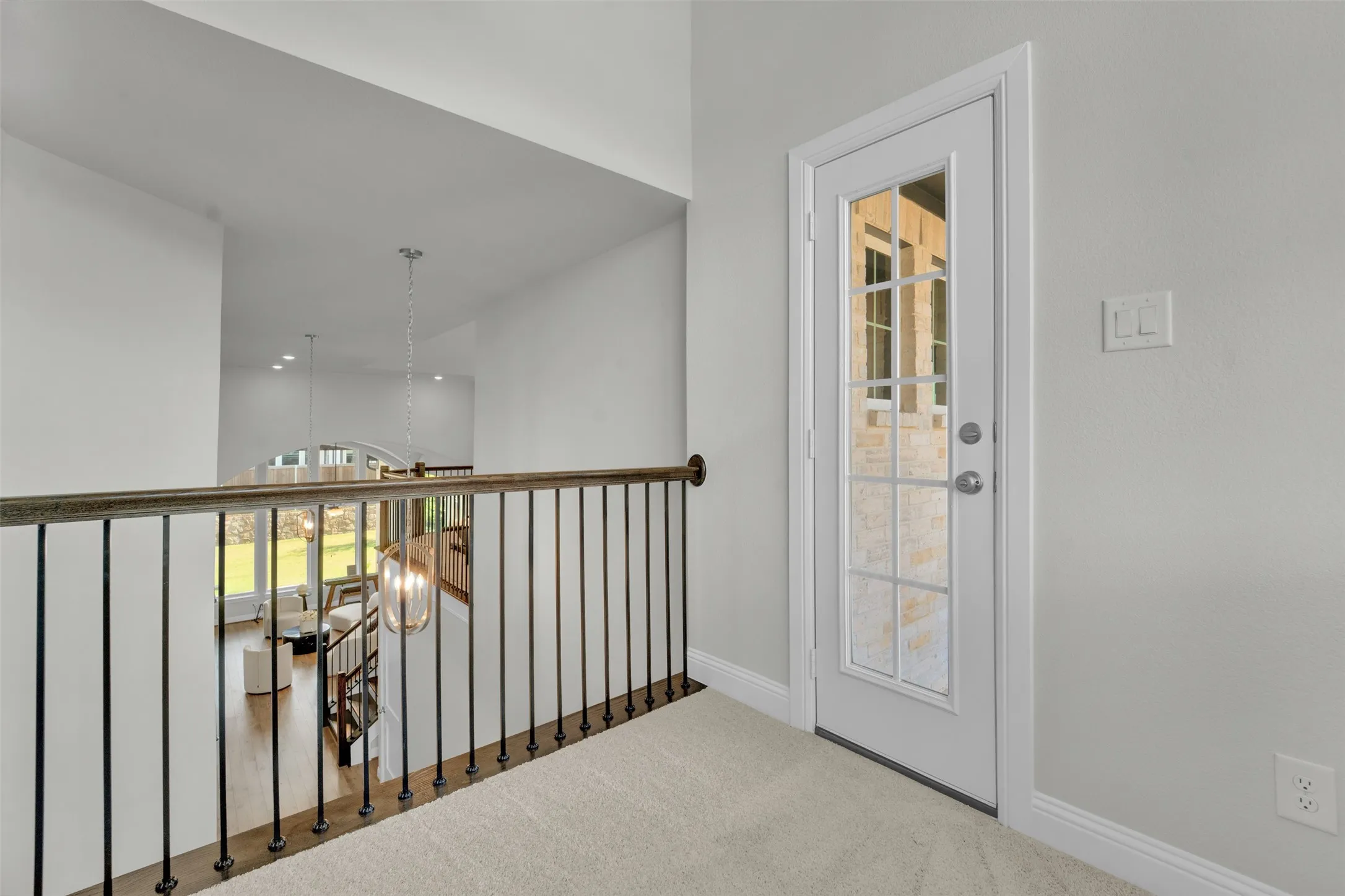 Upper-level landing with carpet flooring, metal balusters, and a glass-paneled door