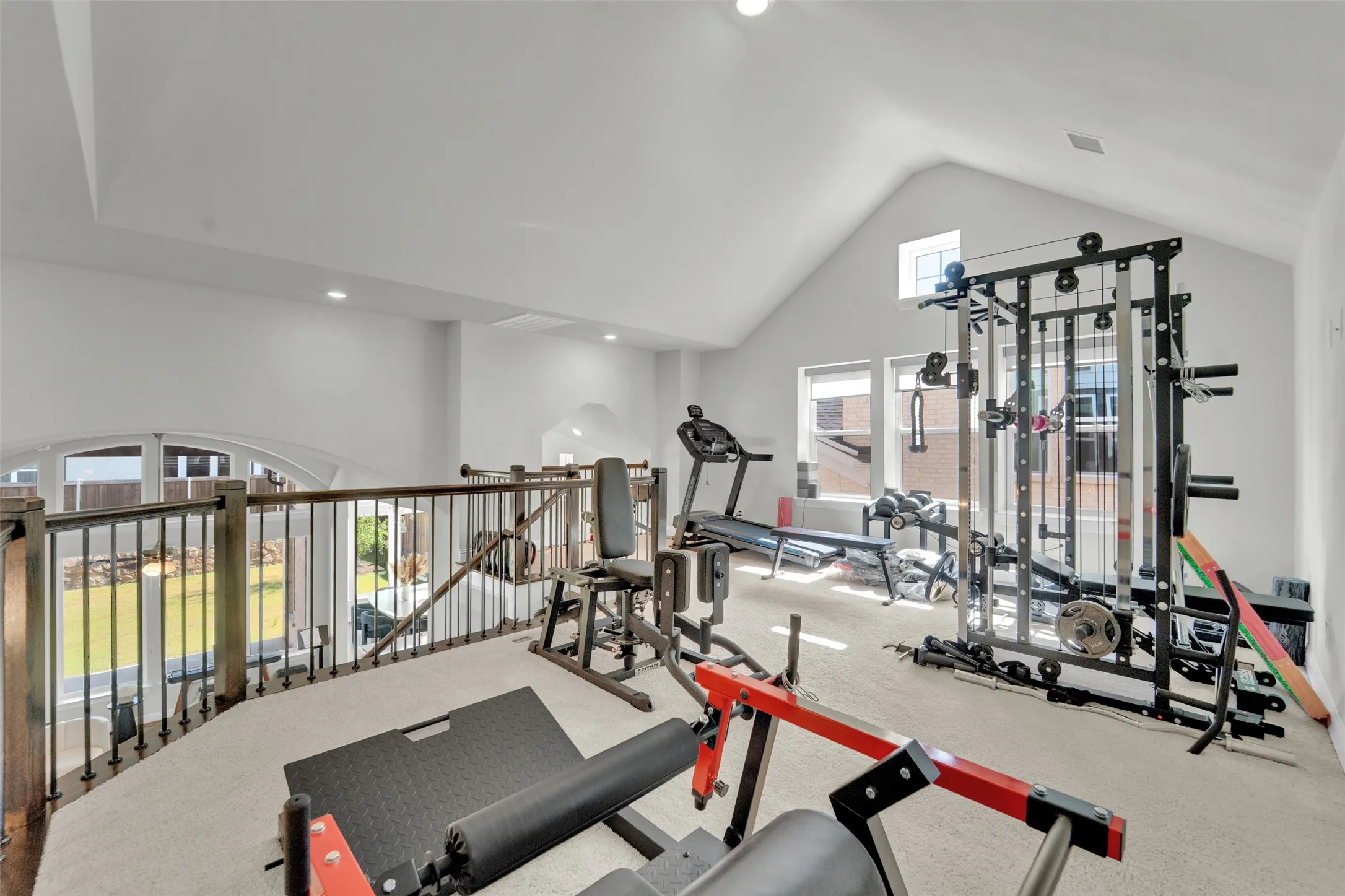 Vaulted ceiling with recessed lighting, carpeting, and a wrought iron and wood railing