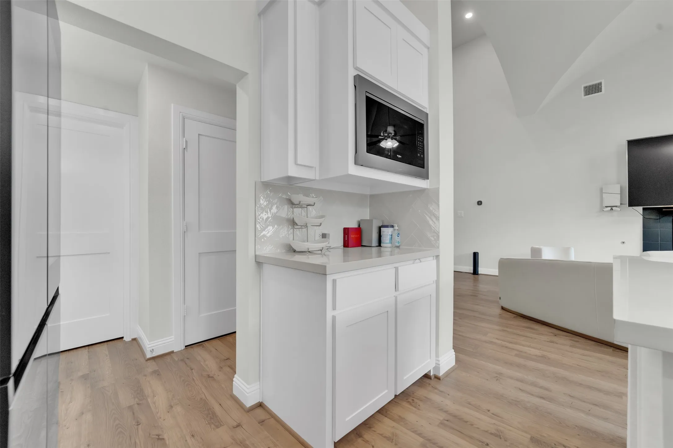 Integrated beverage station featuring white cabinetry, a built-in microwave, light-toned countertop, and patterned tile backsplash