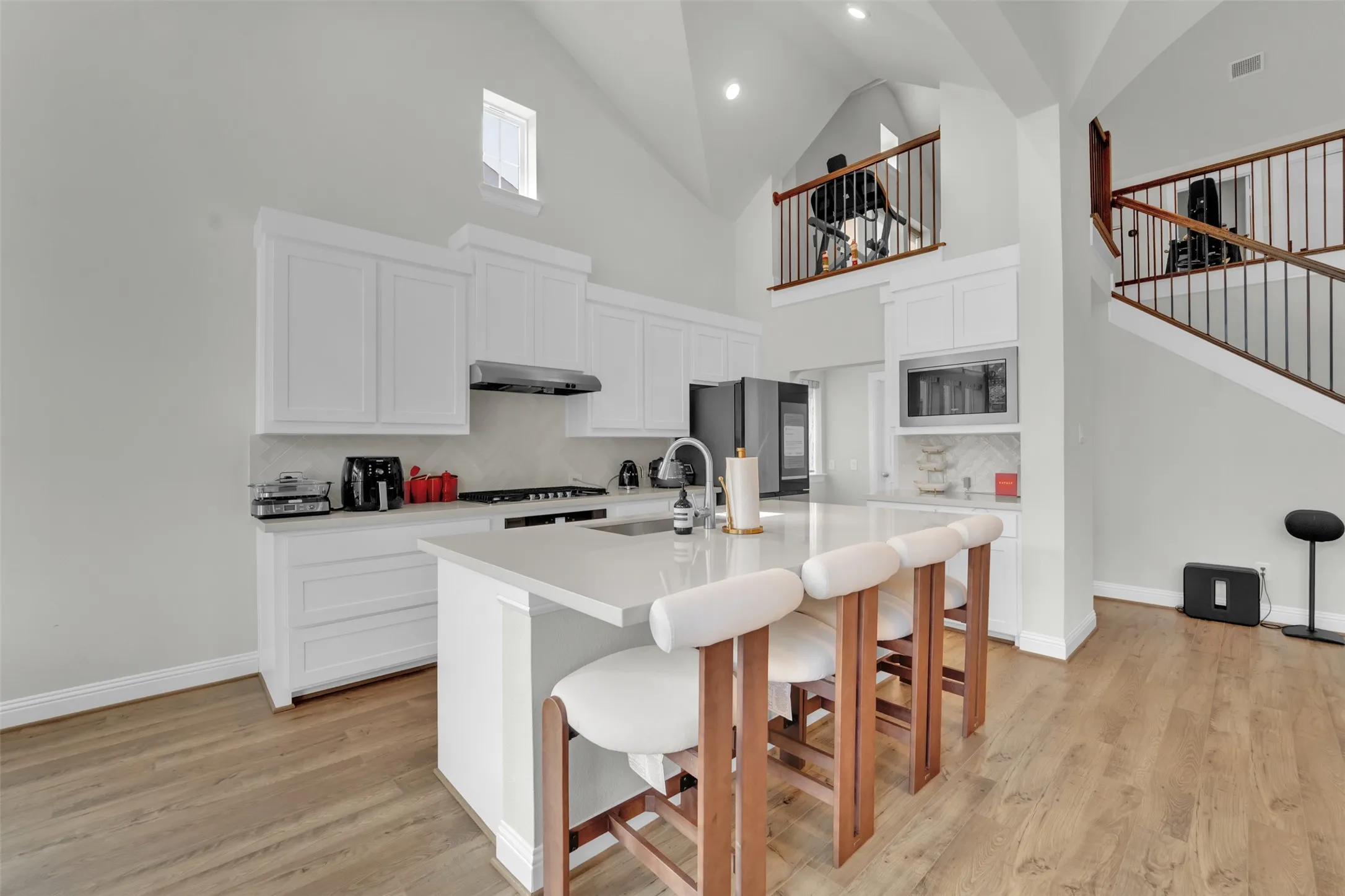 Kitchen featuring a large island with counter seating, white cabinetry, integrated stainless steel appliances, and wood-finish flooring
