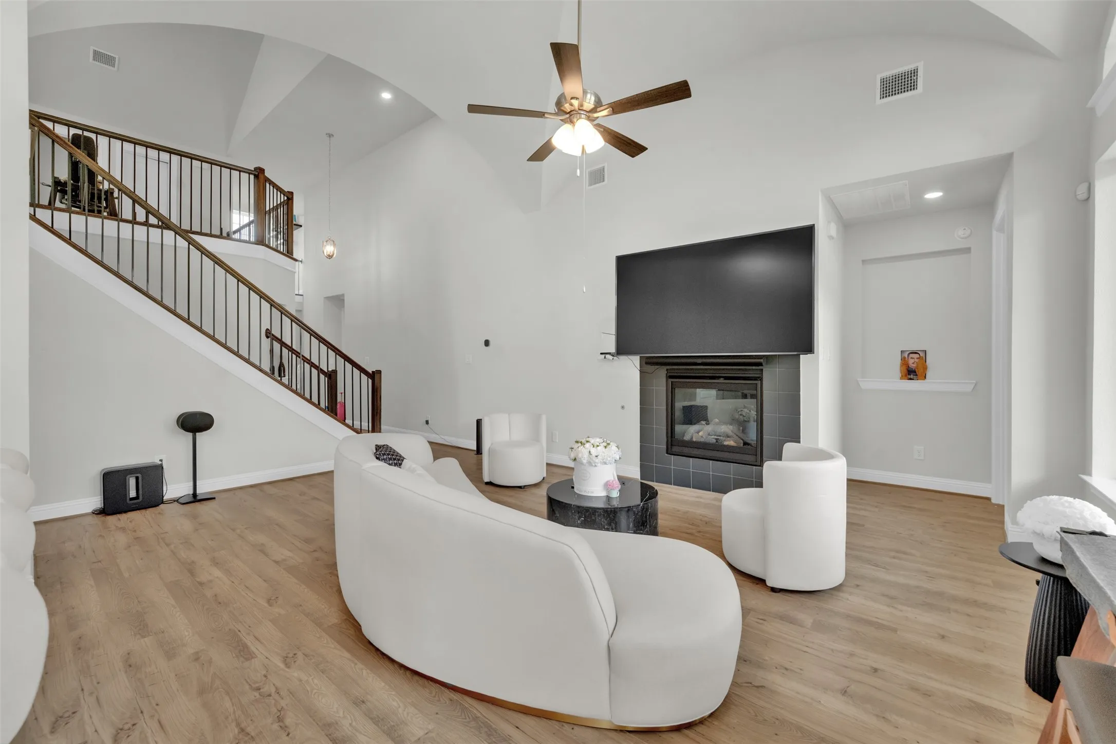 Vaulted ceiling, wood-finish flooring, staircase with wood railings, fireplace with dark tile surround, and ceiling fan
