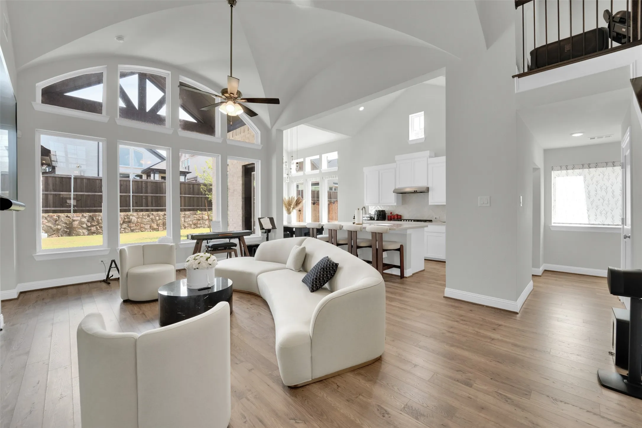 Vaulted ceiling, wood-finish flooring, white cabinetry, integrated range hood, and a ceiling fan with light fixture