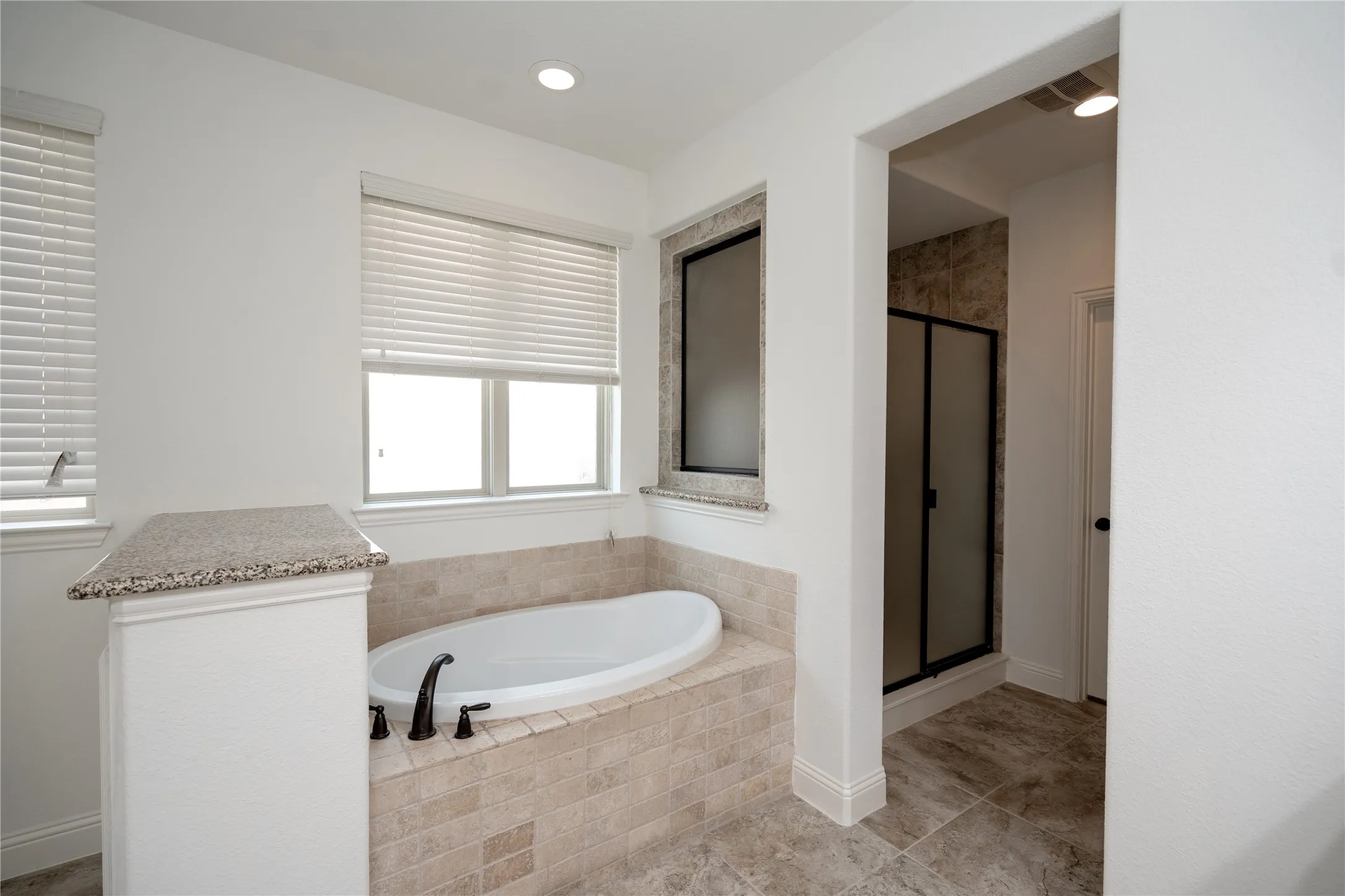 Recessed bathtub with tile surround, dual windows, granite-finish ledges, and a separate shower enclosure with frosted glass