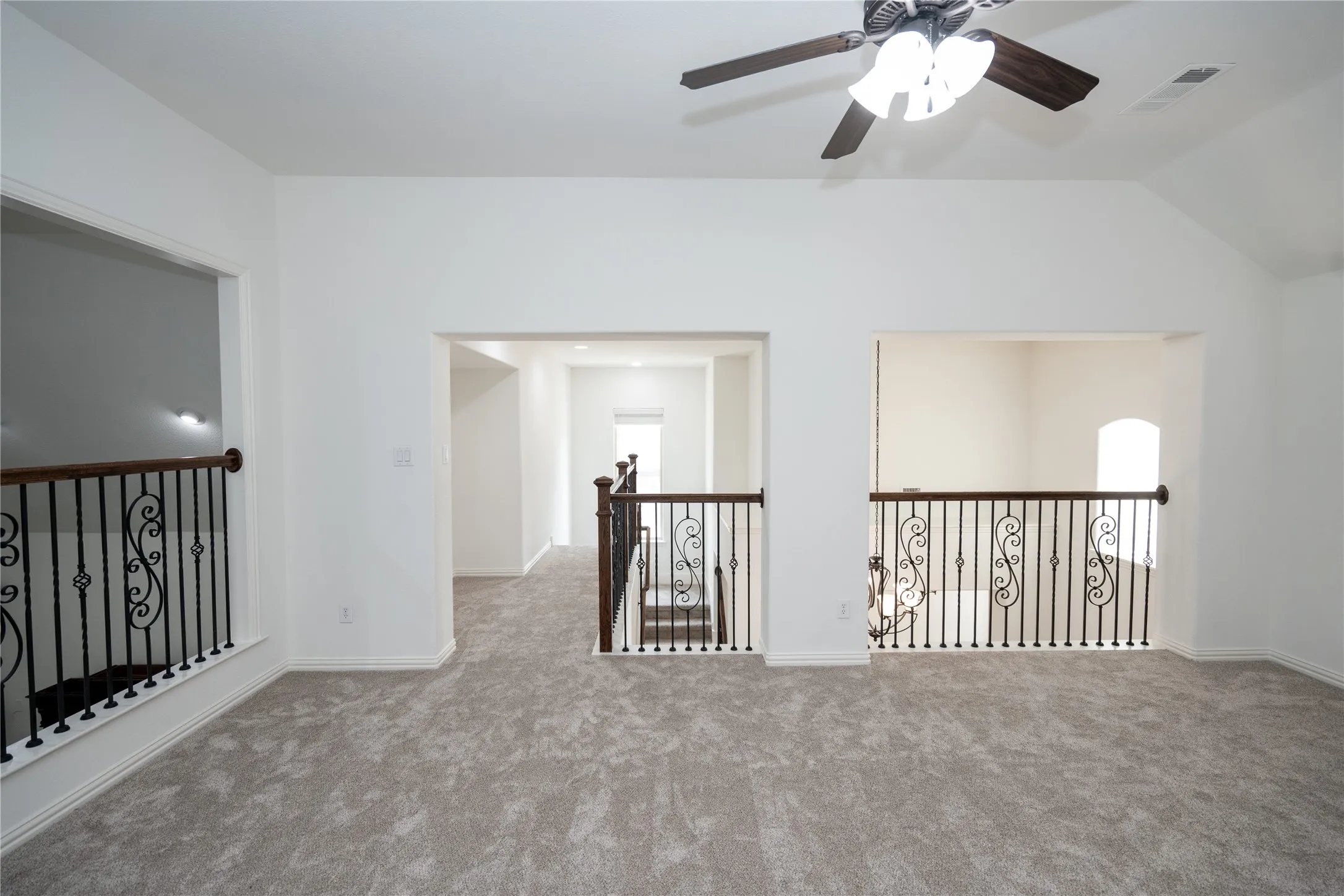 Vaulted ceiling with a ceiling fan, carpeted flooring, and decorative wrought iron railings