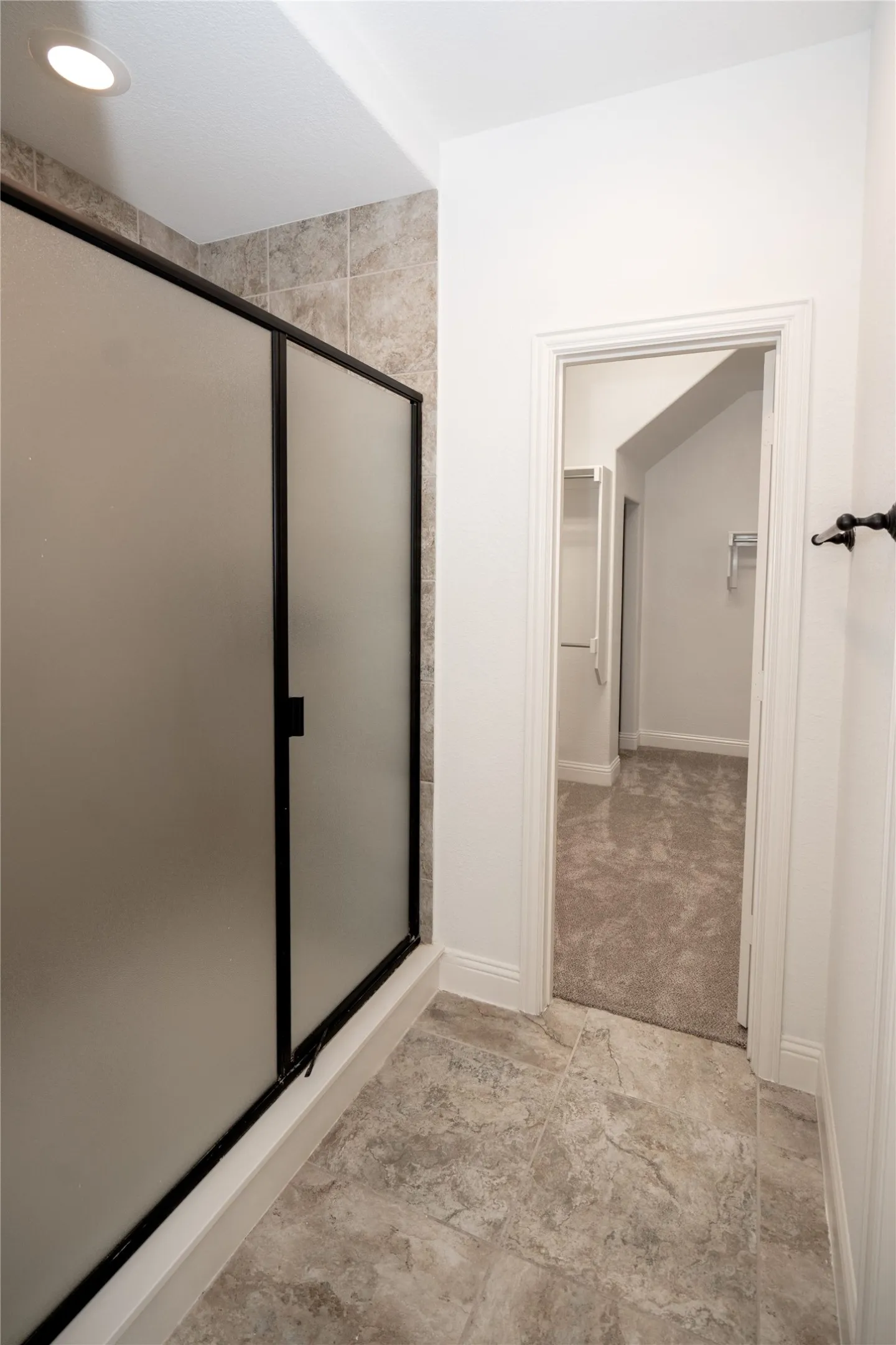 Shower enclosure with frosted glass and black frame, recessed lighting, and tile flooring