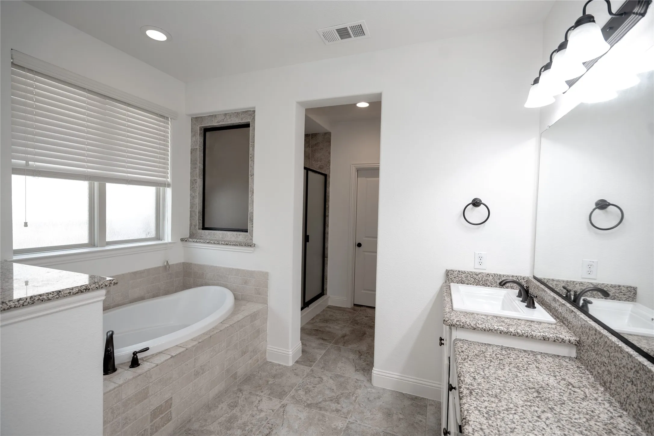 Bathroom featuring a built-in tub with tile surround, a dual vanity with granite countertops, and a walk-in shower with a glass enclosure