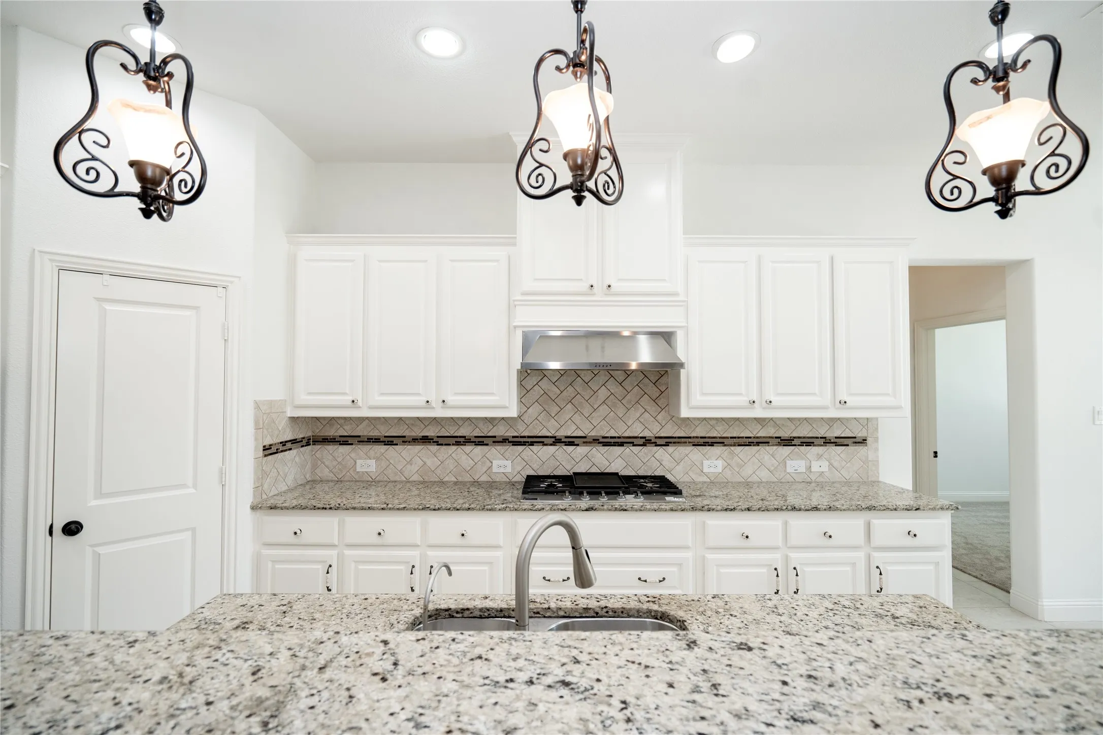 Kitchen featuring an island with a stainless steel sink and faucet, white cabinetry, granite countertops, and a herringbone tile backsplash