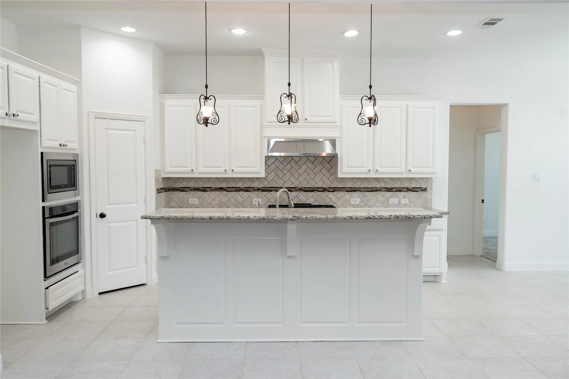Kitchen featuring a central island with an integrated sink, white cabinetry, a herringbone tile backsplash, stainless steel appliances, and pendant lighting