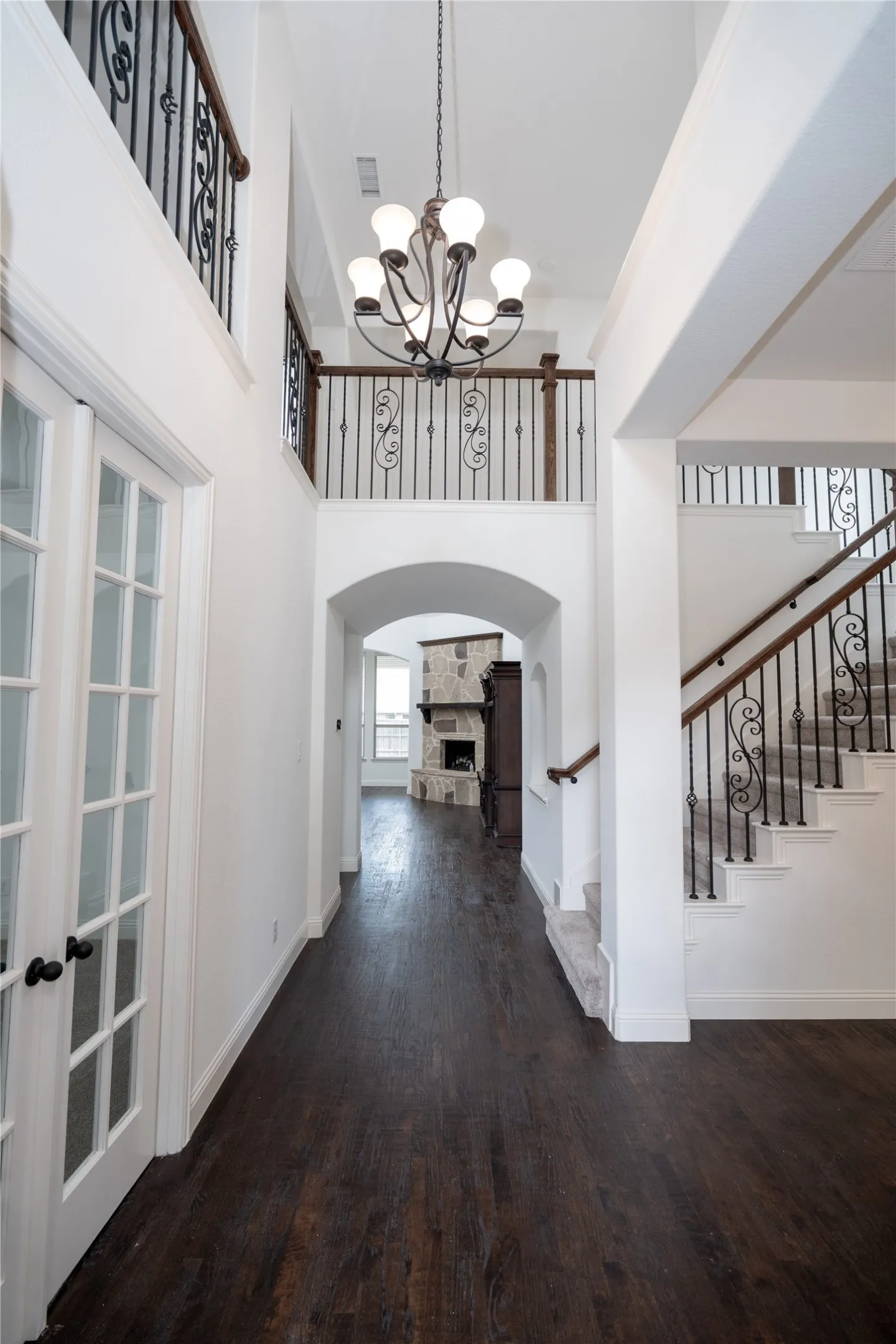 Double-height entryway with wood-finish flooring, an arched doorway, and a chandelier