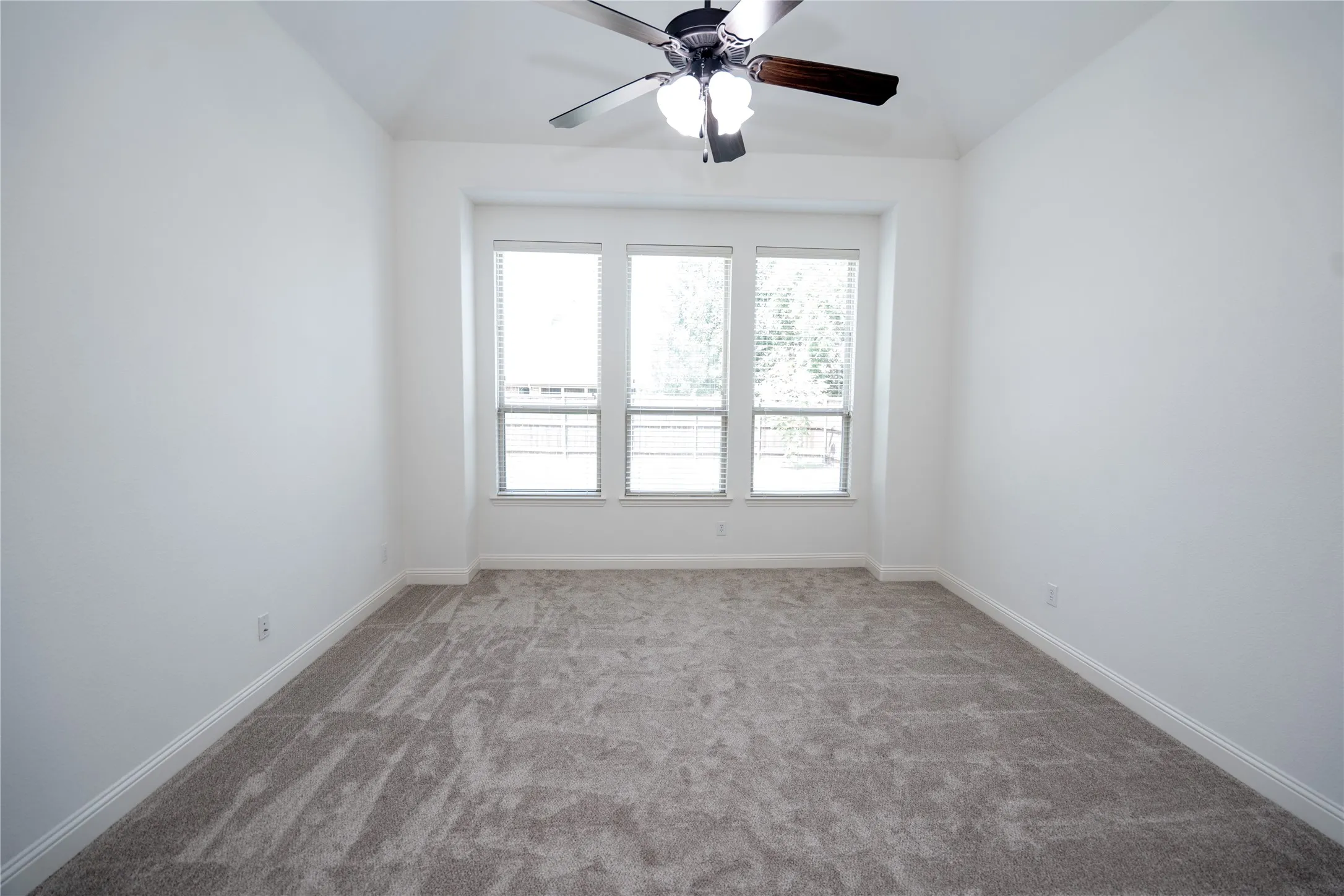 Recessed window bay, gray carpet, multiple windows with blinds, ceiling fan with light fixture, and white wall finishes