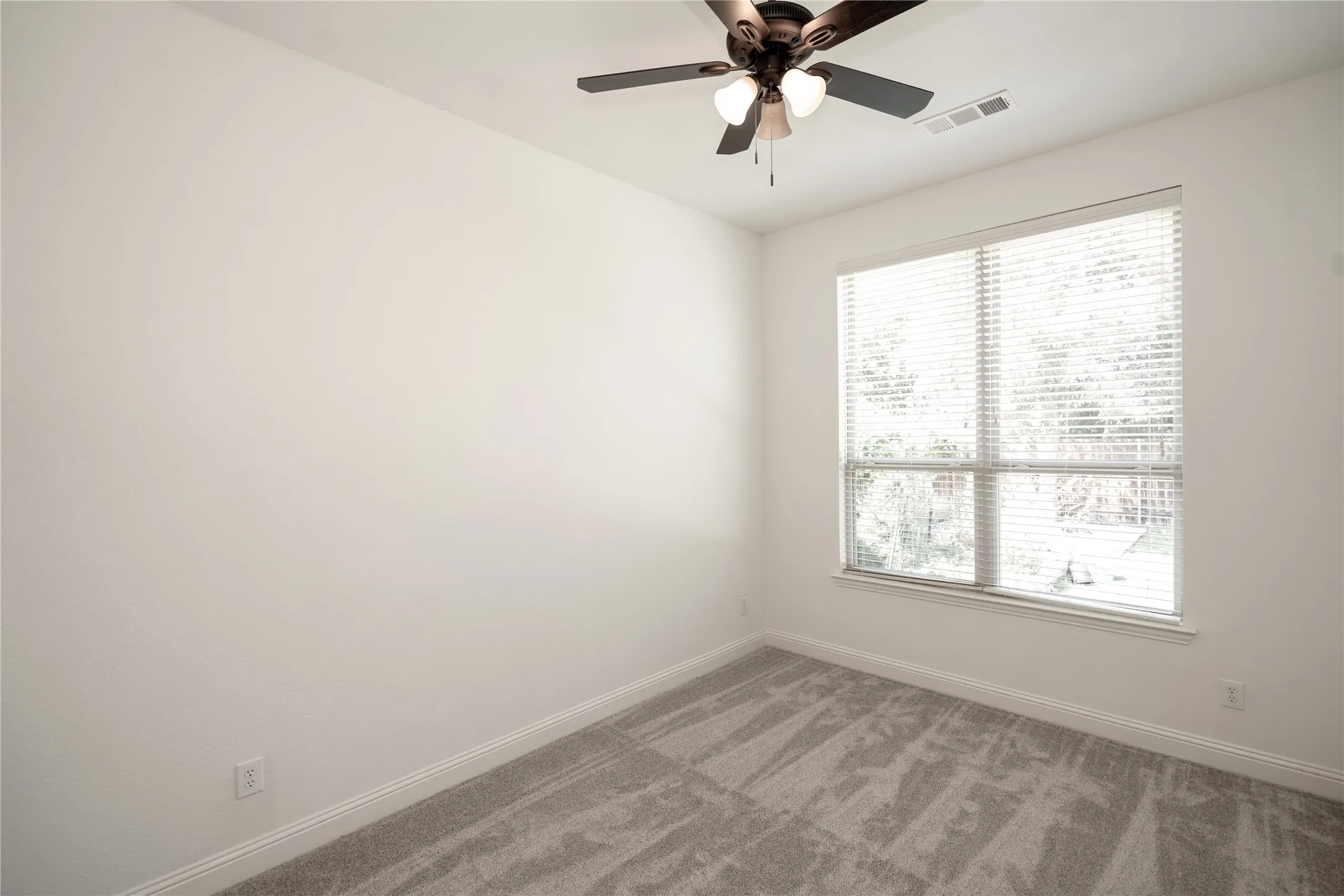 Window with blinds, ceiling fan with integrated lighting, and neutral carpeting