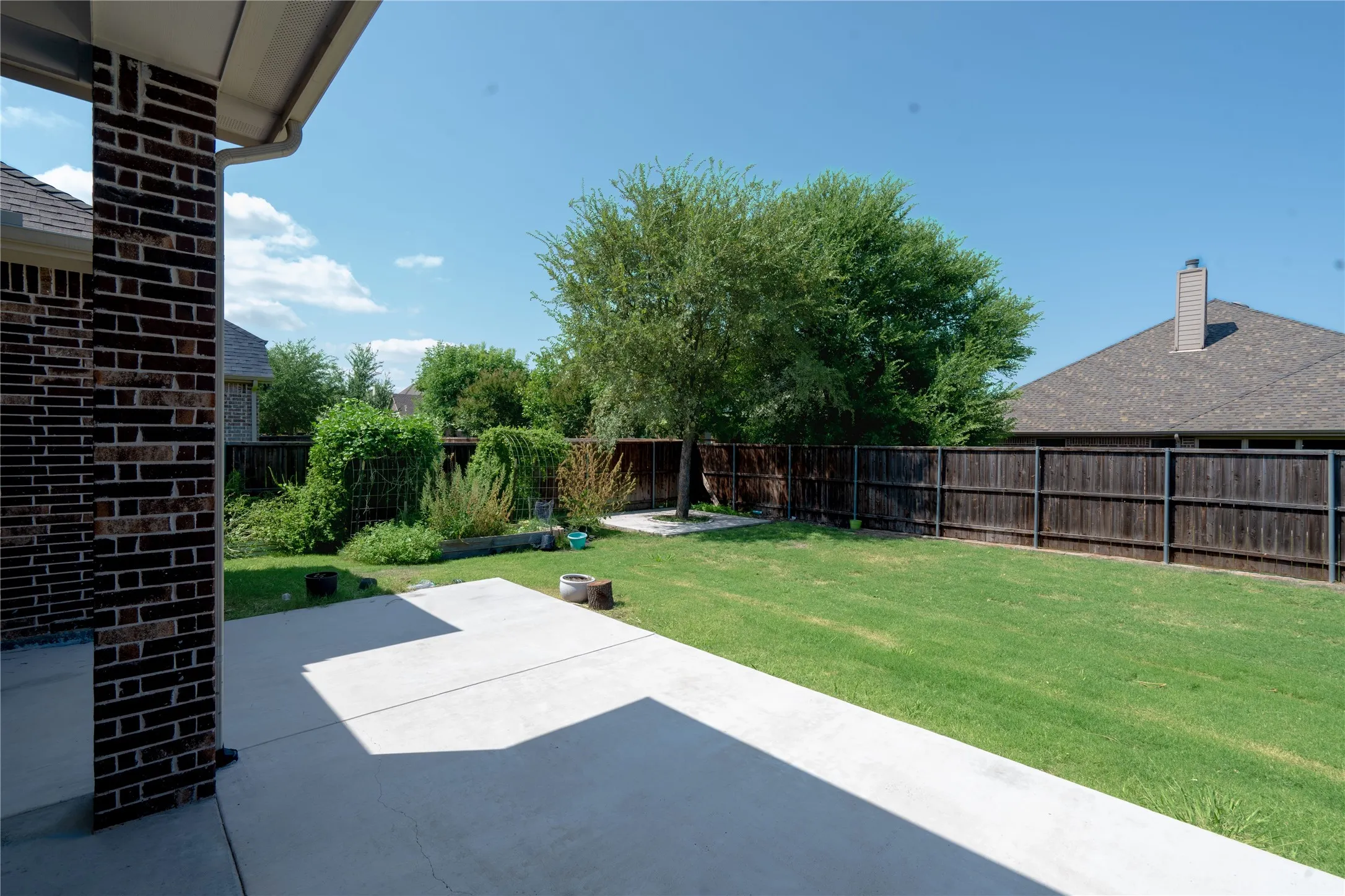 Expansive concrete patio with a brick support column, a wood privacy fence, and a manicured lawn