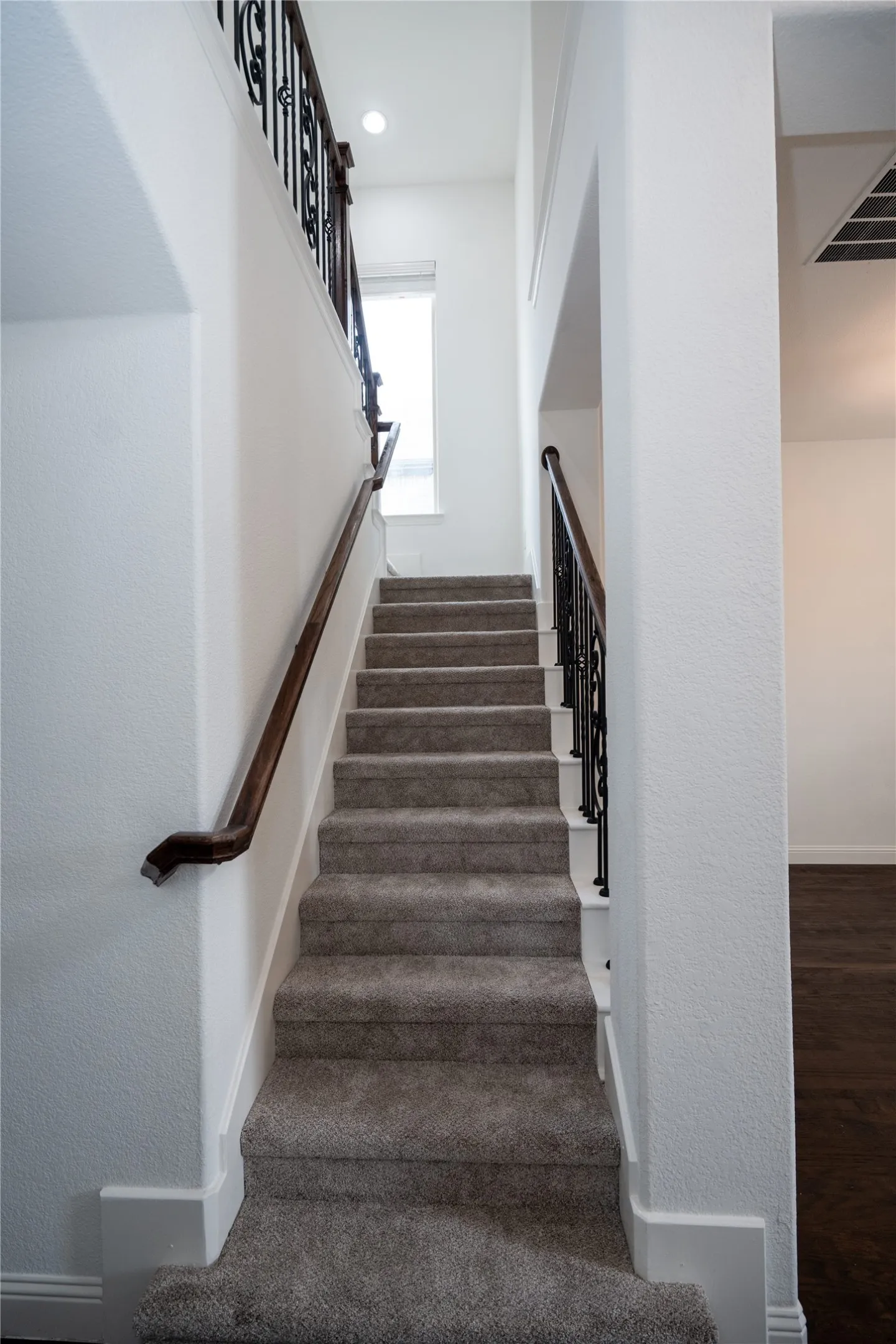 Carpeted staircase featuring wrought iron balusters and a dark wood handrail
