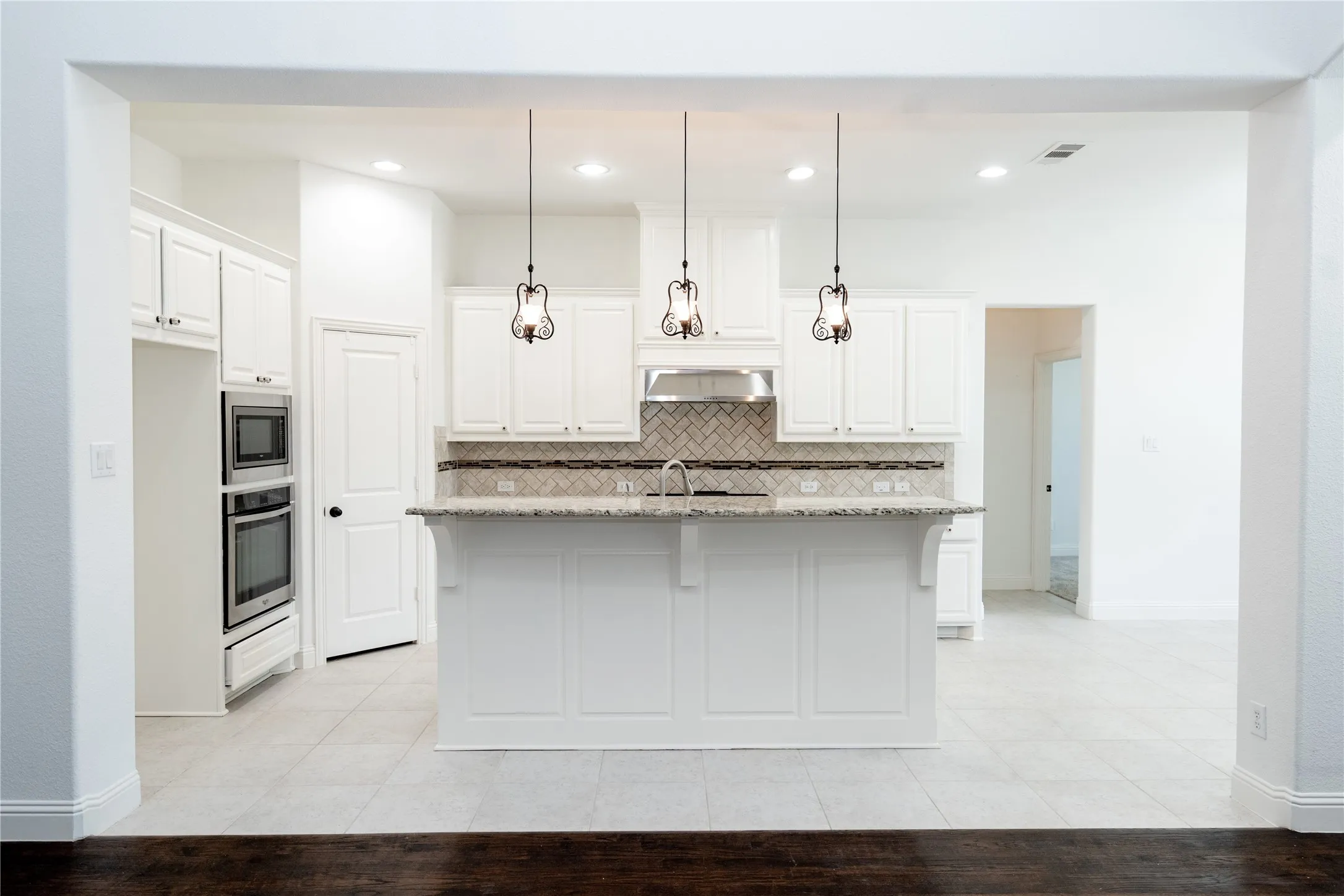 White cabinetry with stainless steel appliances, a kitchen island with pendant lighting, a tile backsplash, and light-toned tile flooring