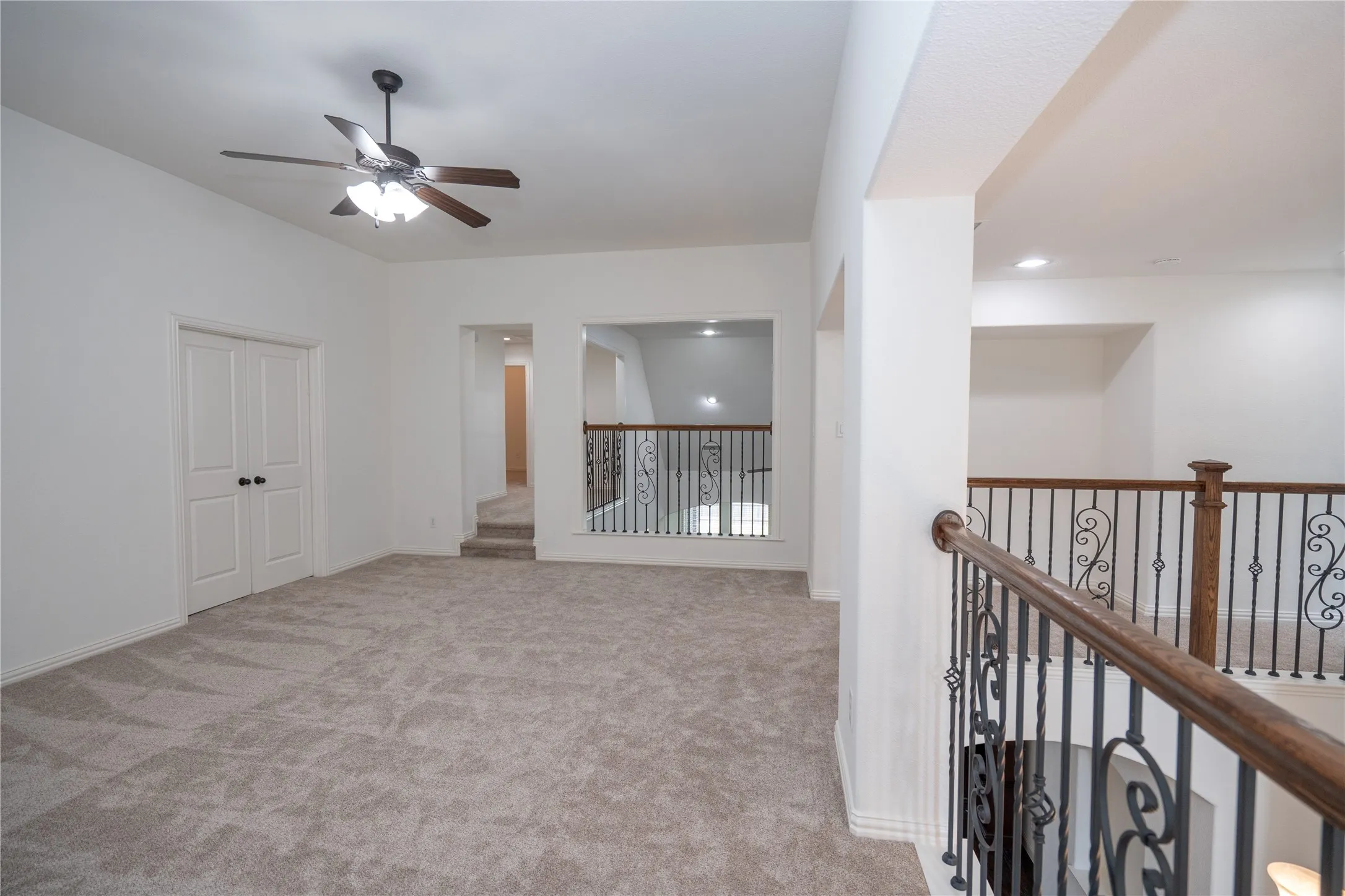 Carpeted open area with ceiling fan, recessed lighting, and wrought iron balusters