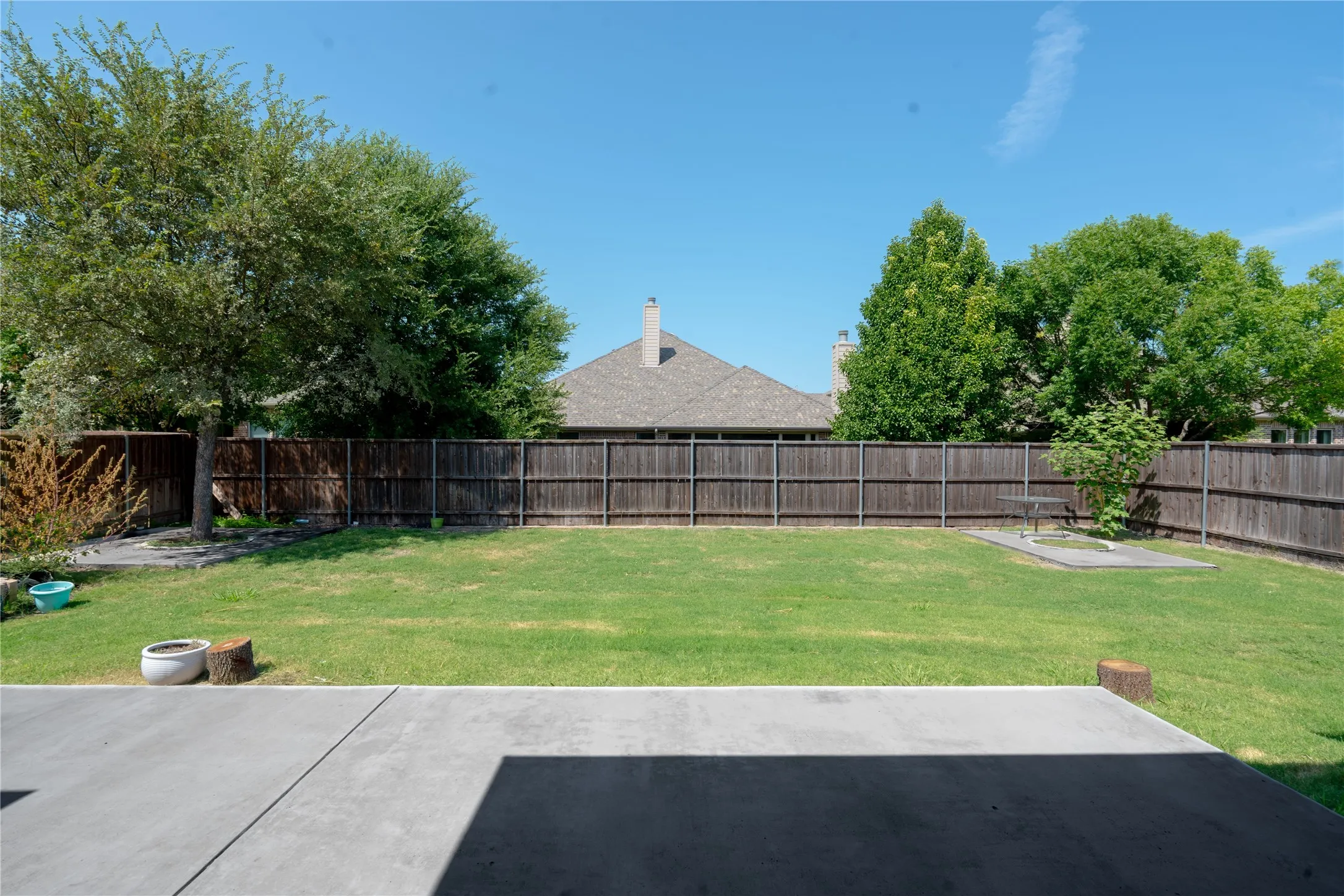 Expansive backyard featuring a concrete patio, a lush green lawn, mature trees, and a durable wood privacy fence