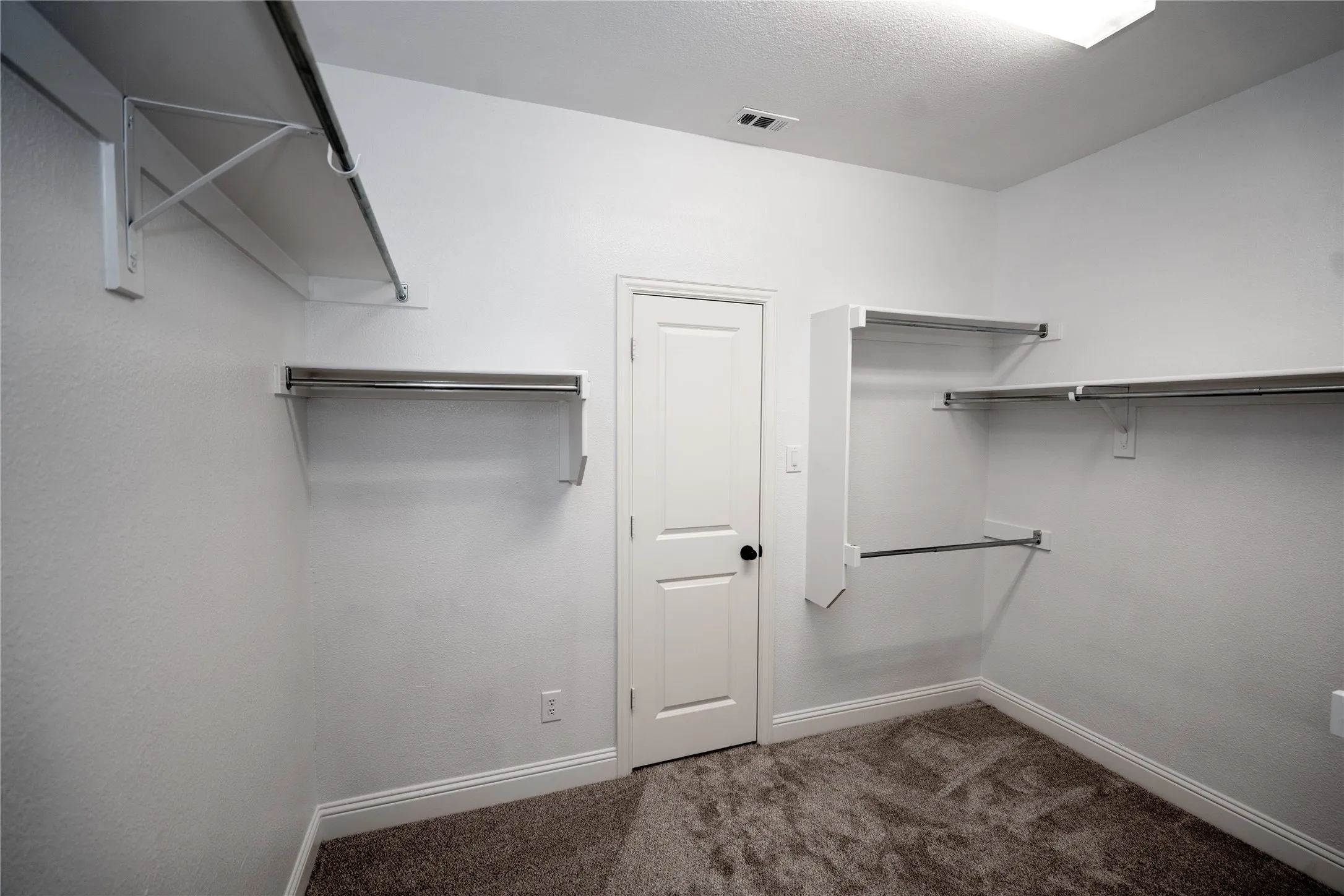 Wall-mounted shelving with integrated hanging rods, carpeted flooring, white trim, and overhead lighting