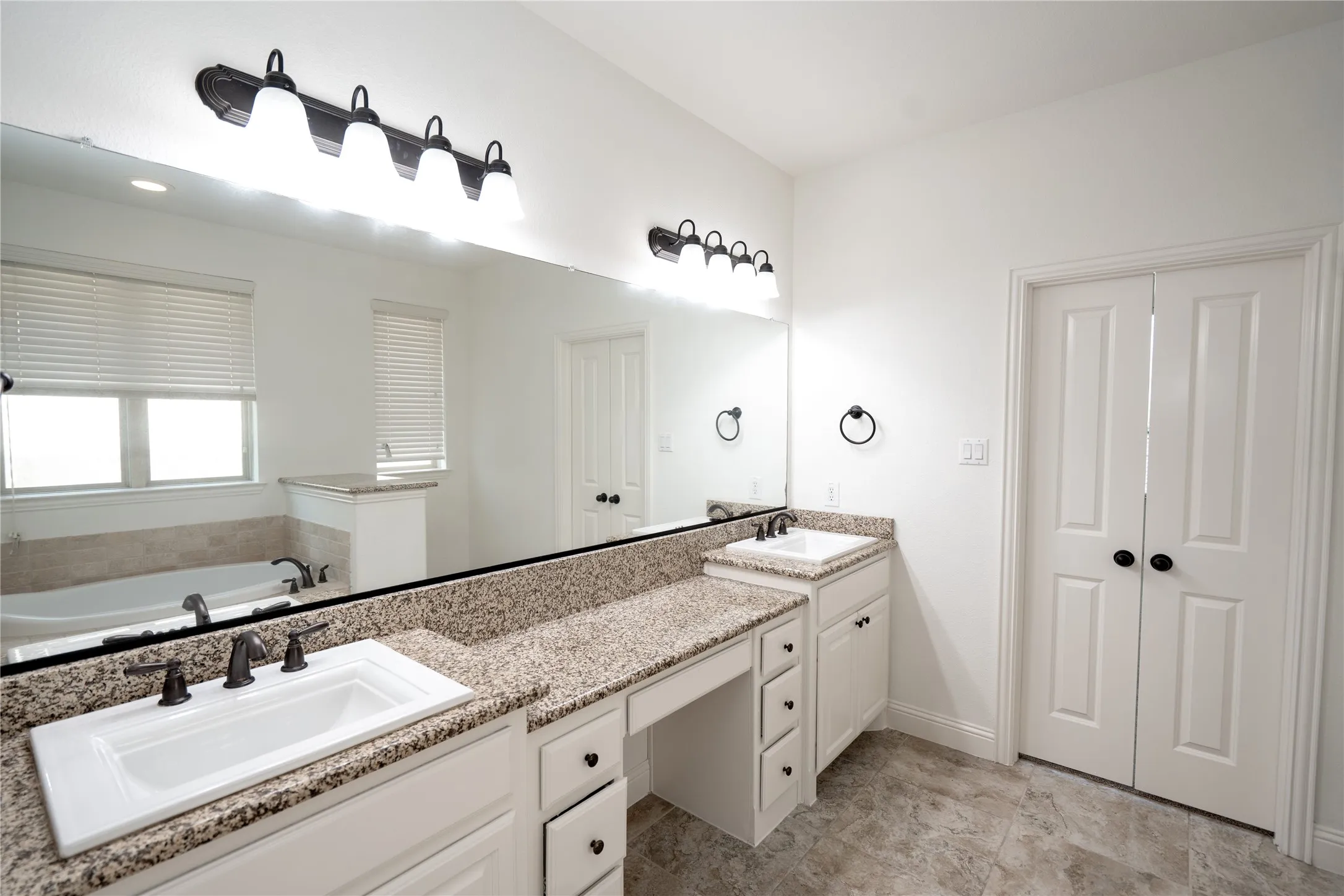 Dual vanity with granite countertops, integrated sinks, white cabinetry, and matte black hardware