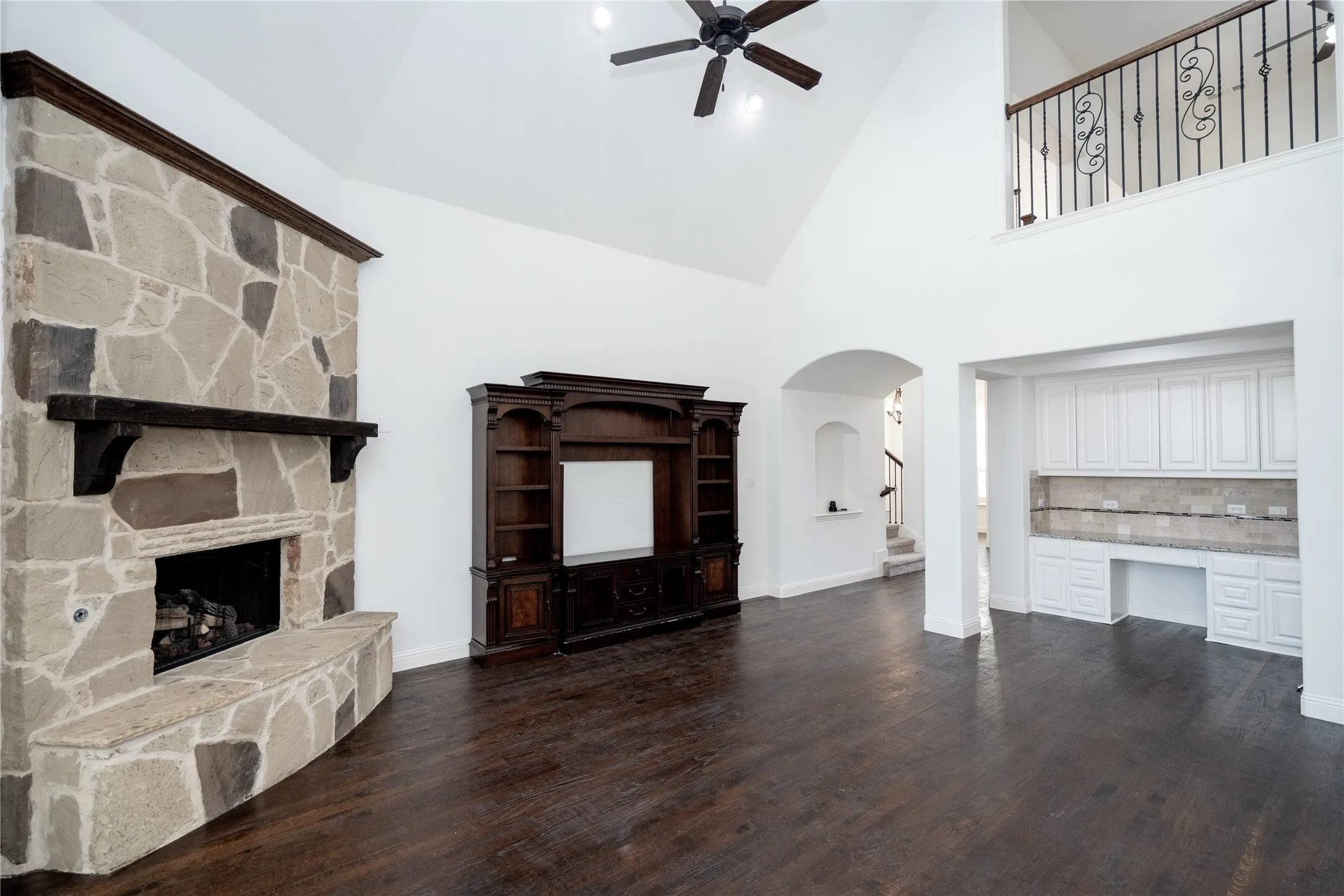 Spacious living area featuring a stone-clad fireplace with mantel, dark wood-finish flooring, and a built-in entertainment center