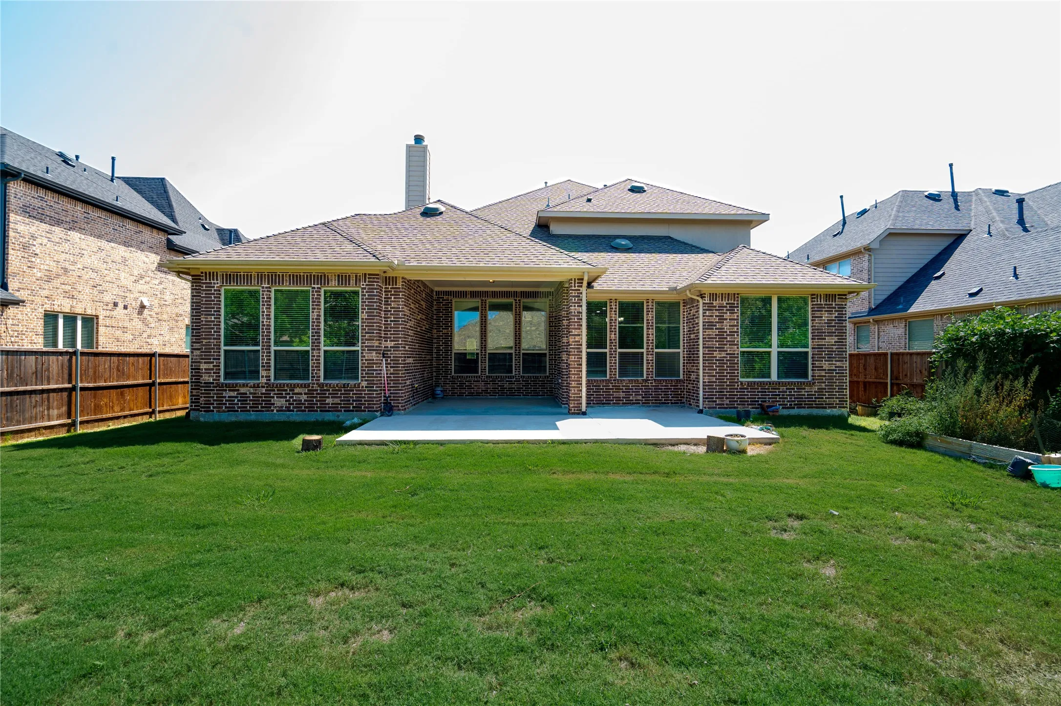 Expansive rear lawn featuring a large concrete patio, brick exterior, and multiple windows