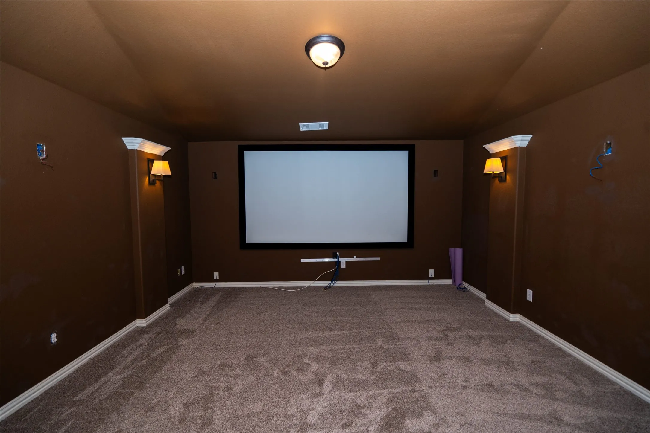 Dedicated media room featuring a large projection screen, built-in wall sconces, and recessed overhead lighting