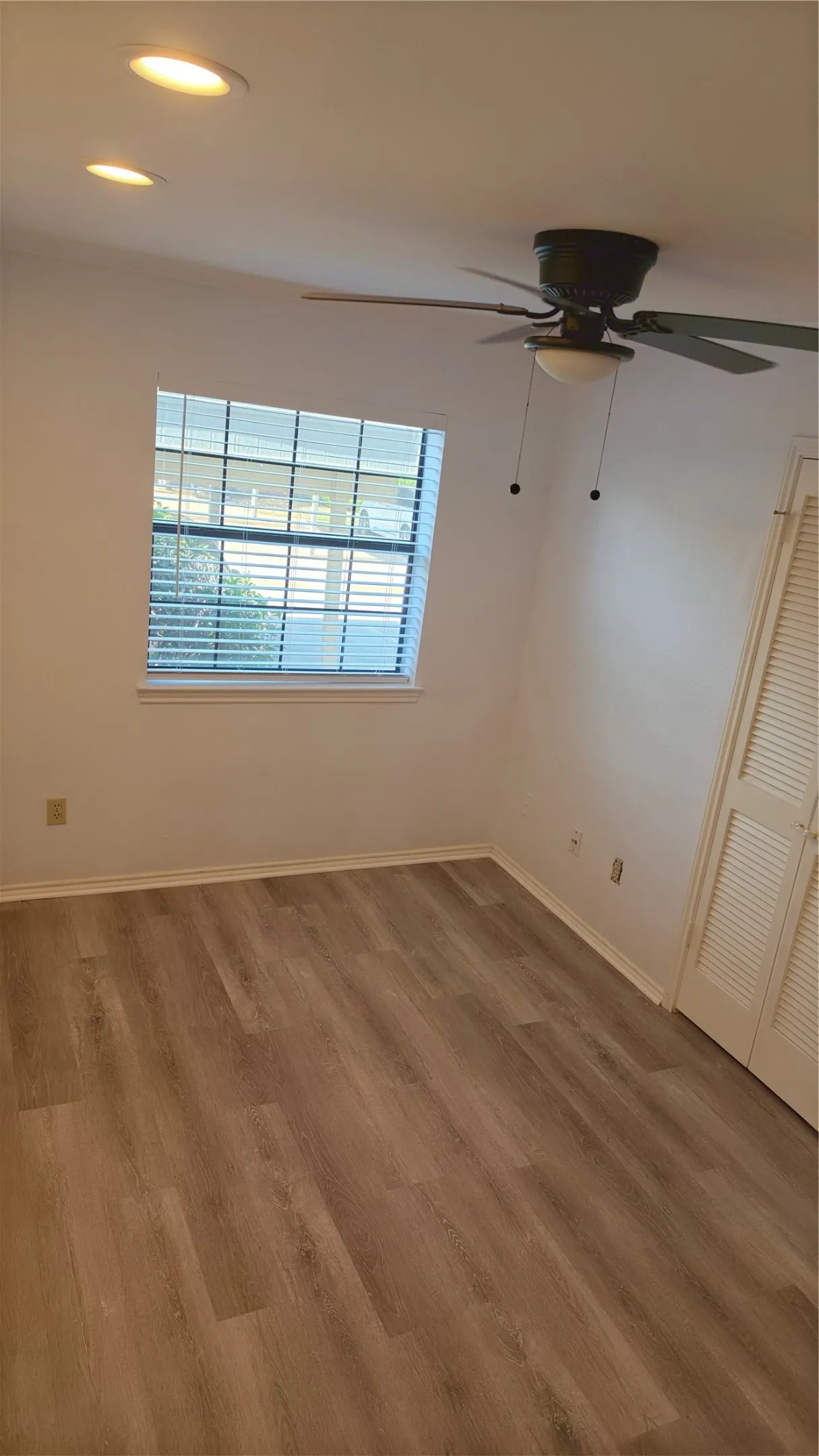 Wood-finish flooring, recessed lighting, ceiling fan with integrated light, louvered bi-fold door, and window with blinds