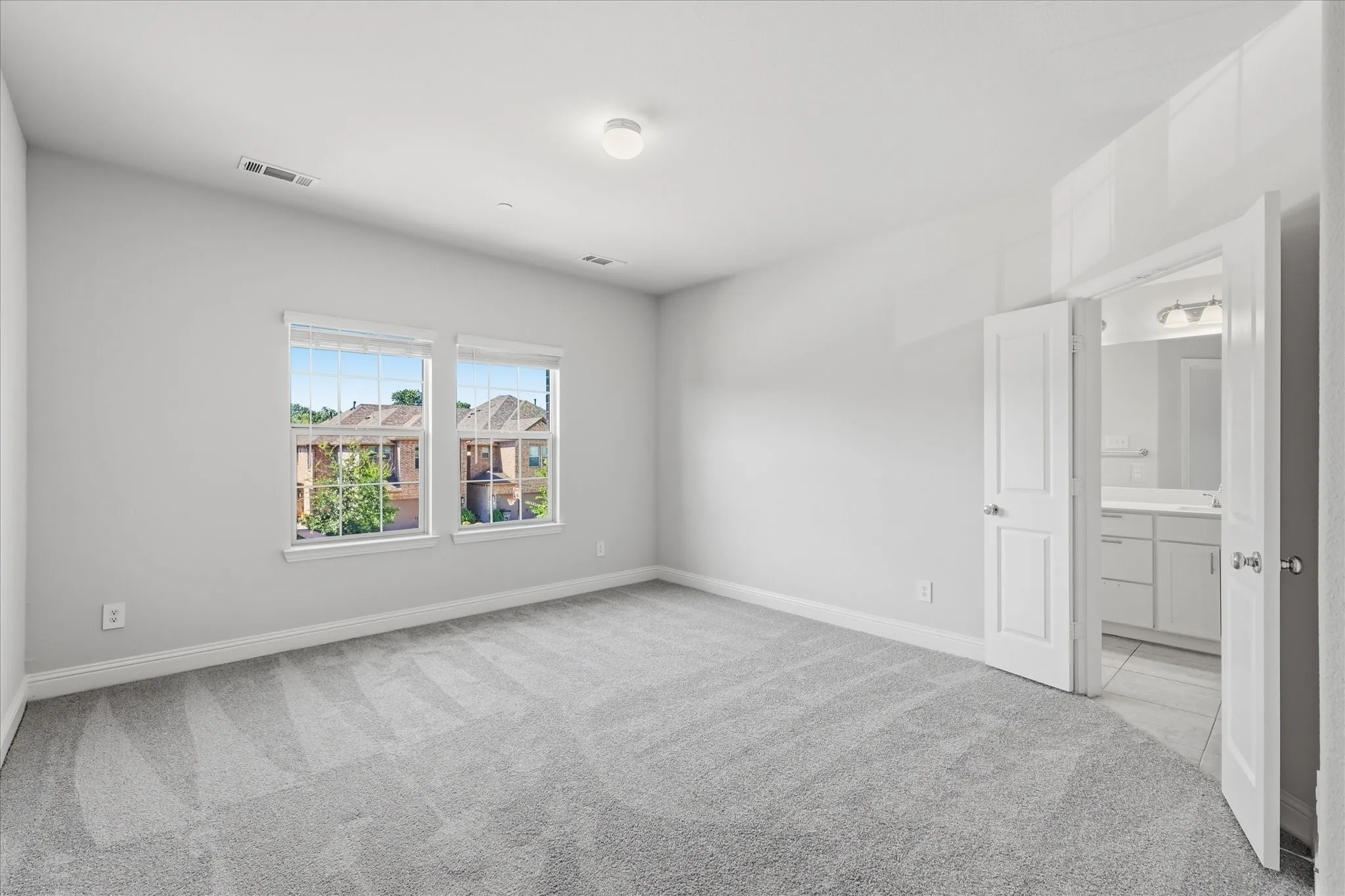 Spacious room featuring light gray carpeting, two windows with blinds, and white trim