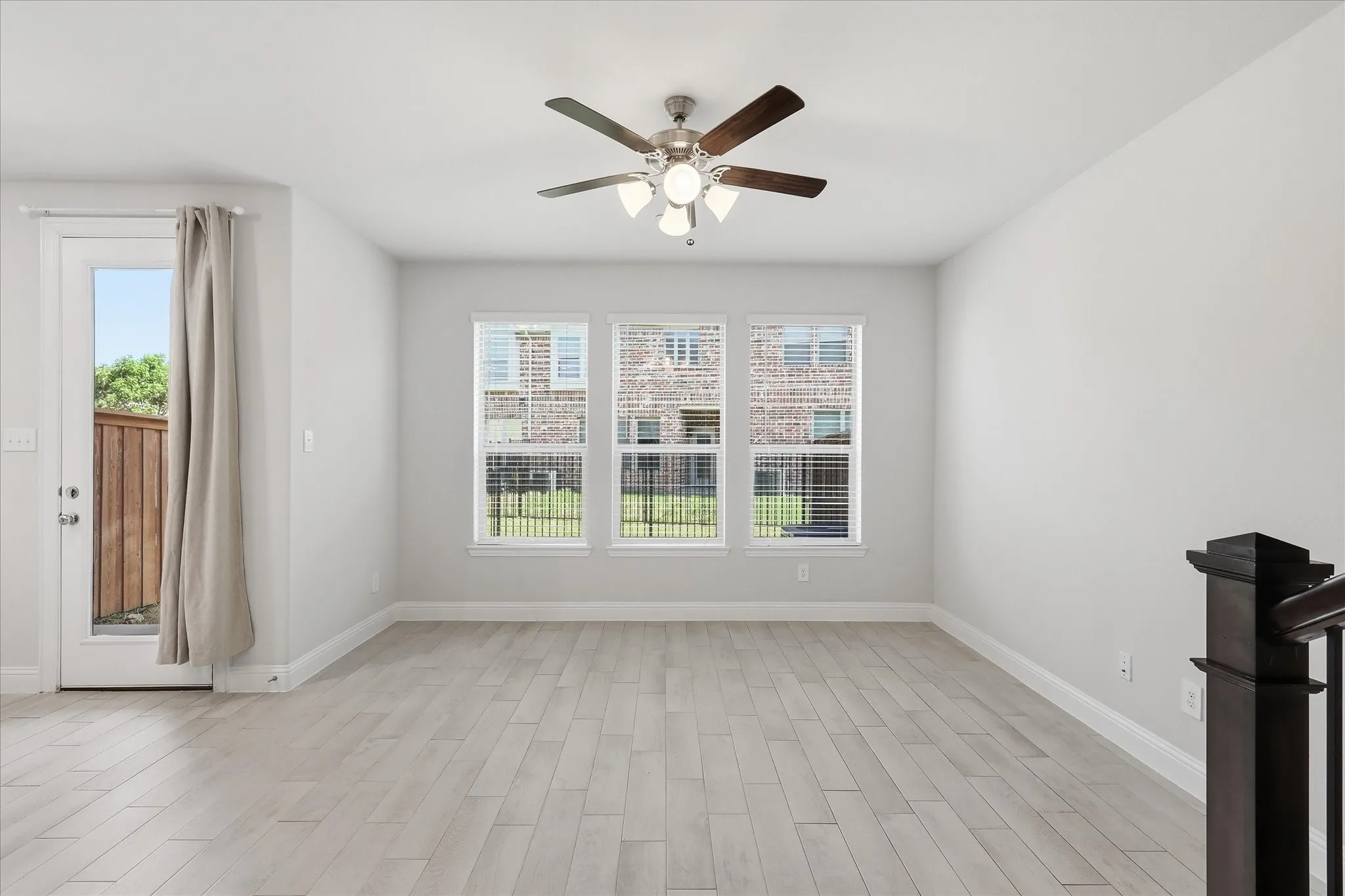 Neutral wall color, wood-finish flooring, ceiling fan with integrated lighting, multiple windows, and a glass-paneled door