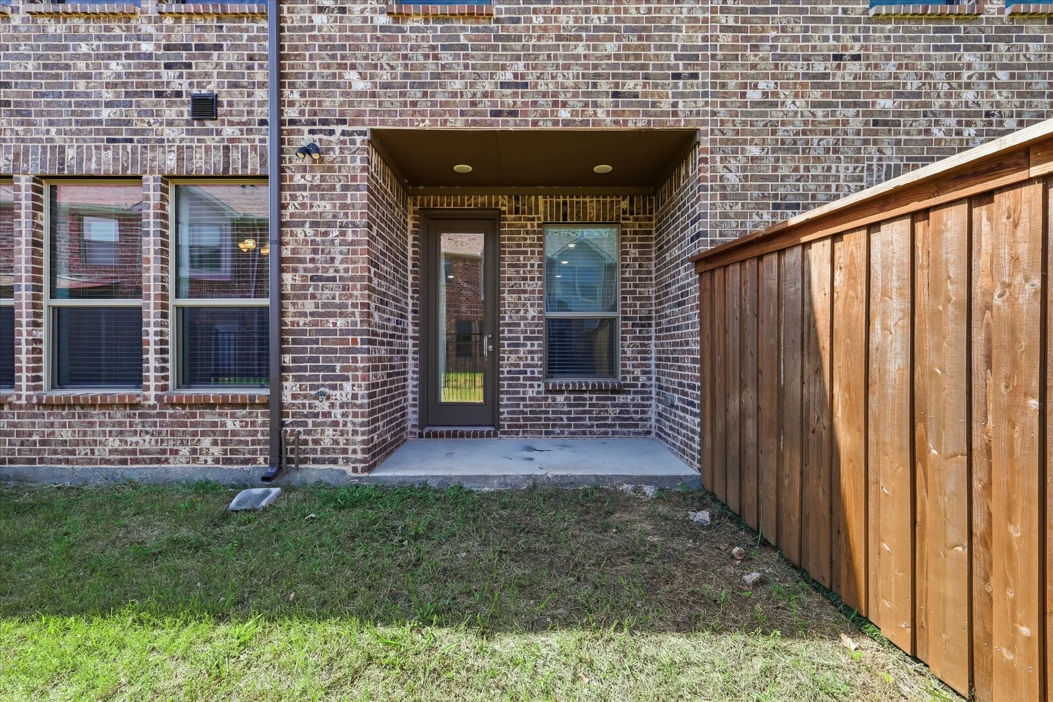 Brick exterior with a covered patio, glass-paneled exterior door, multiple windows, and a wood privacy fence