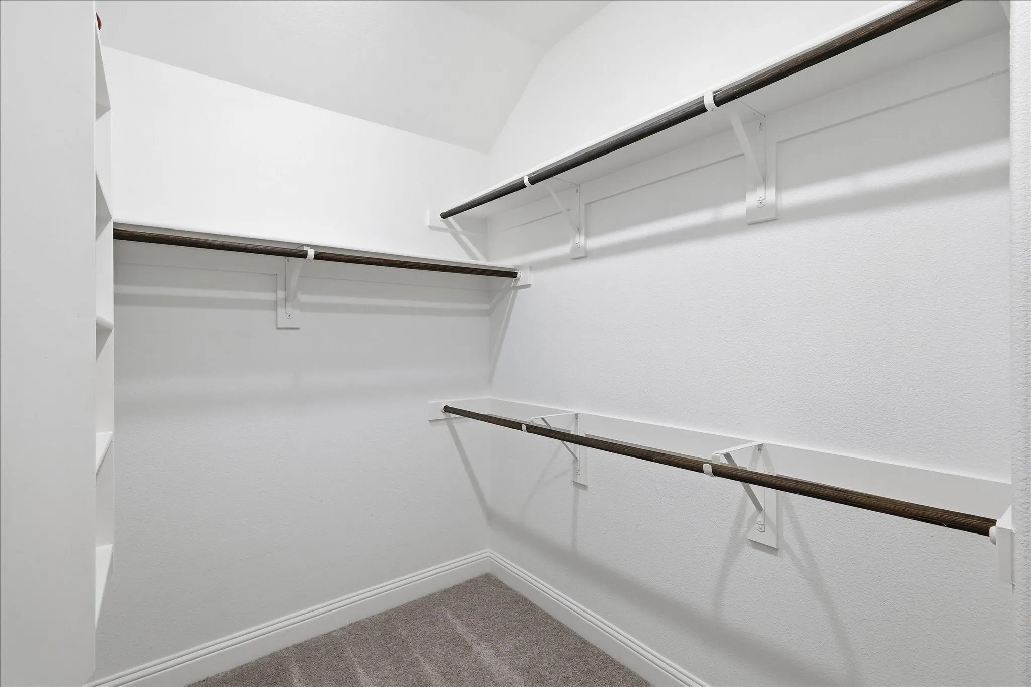 White-painted walls with integrated shelving, dark-finish hanging rods, and gray carpet