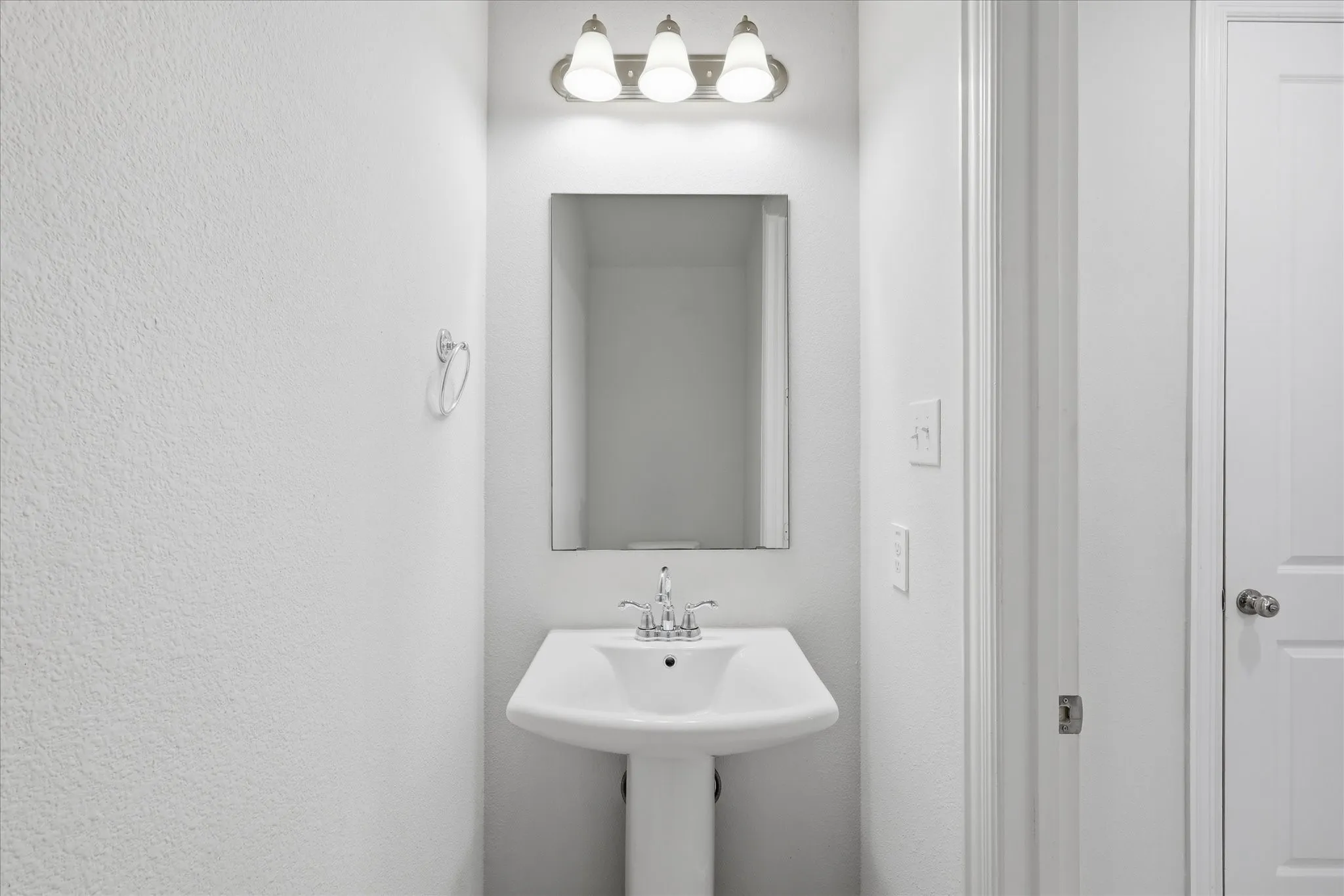 Pedestal sink with chrome faucet, wall-mounted mirror, and vanity light fixture