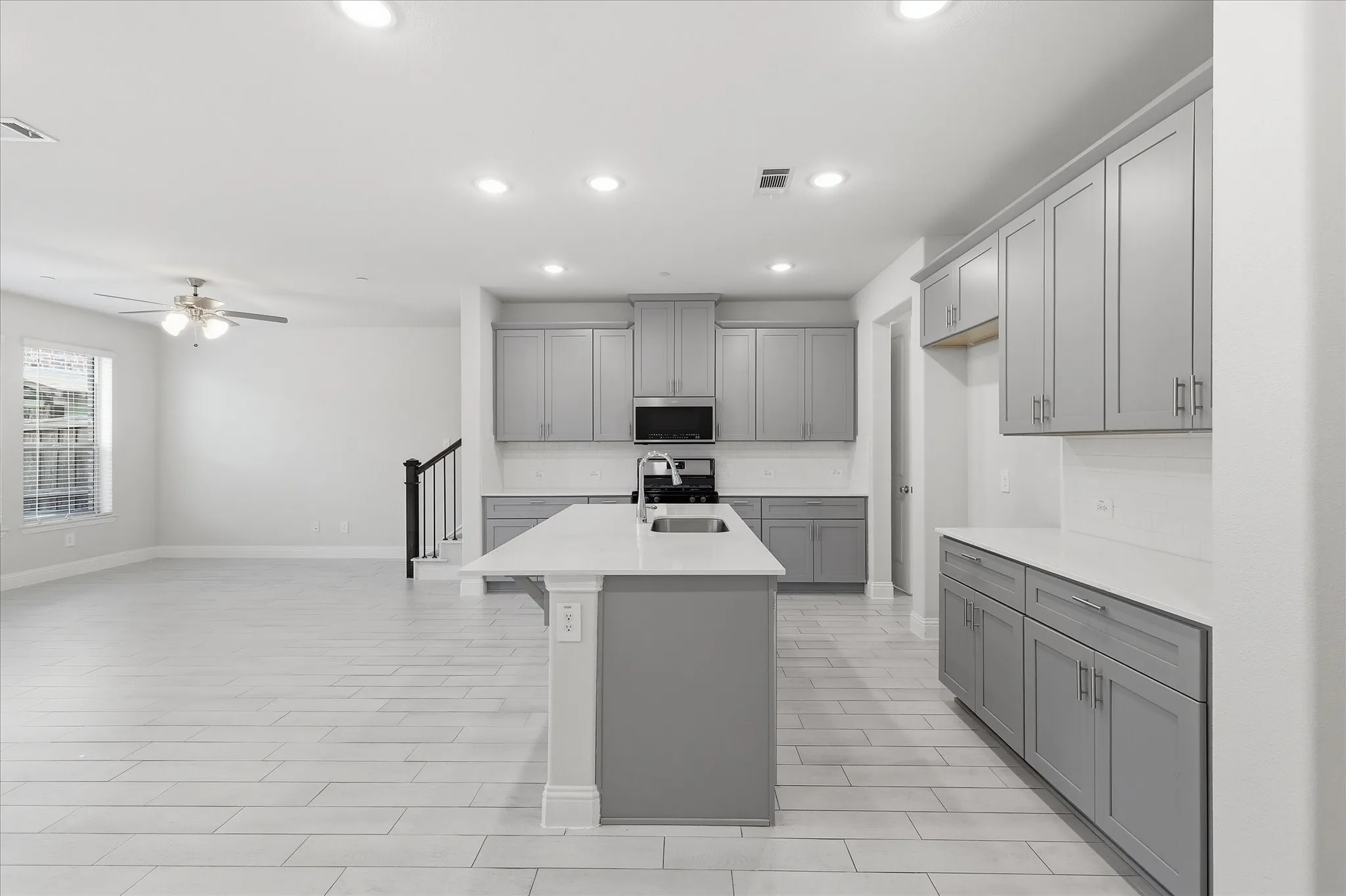 Kitchen featuring a central island with an undermount sink, light gray cabinetry, and light countertops