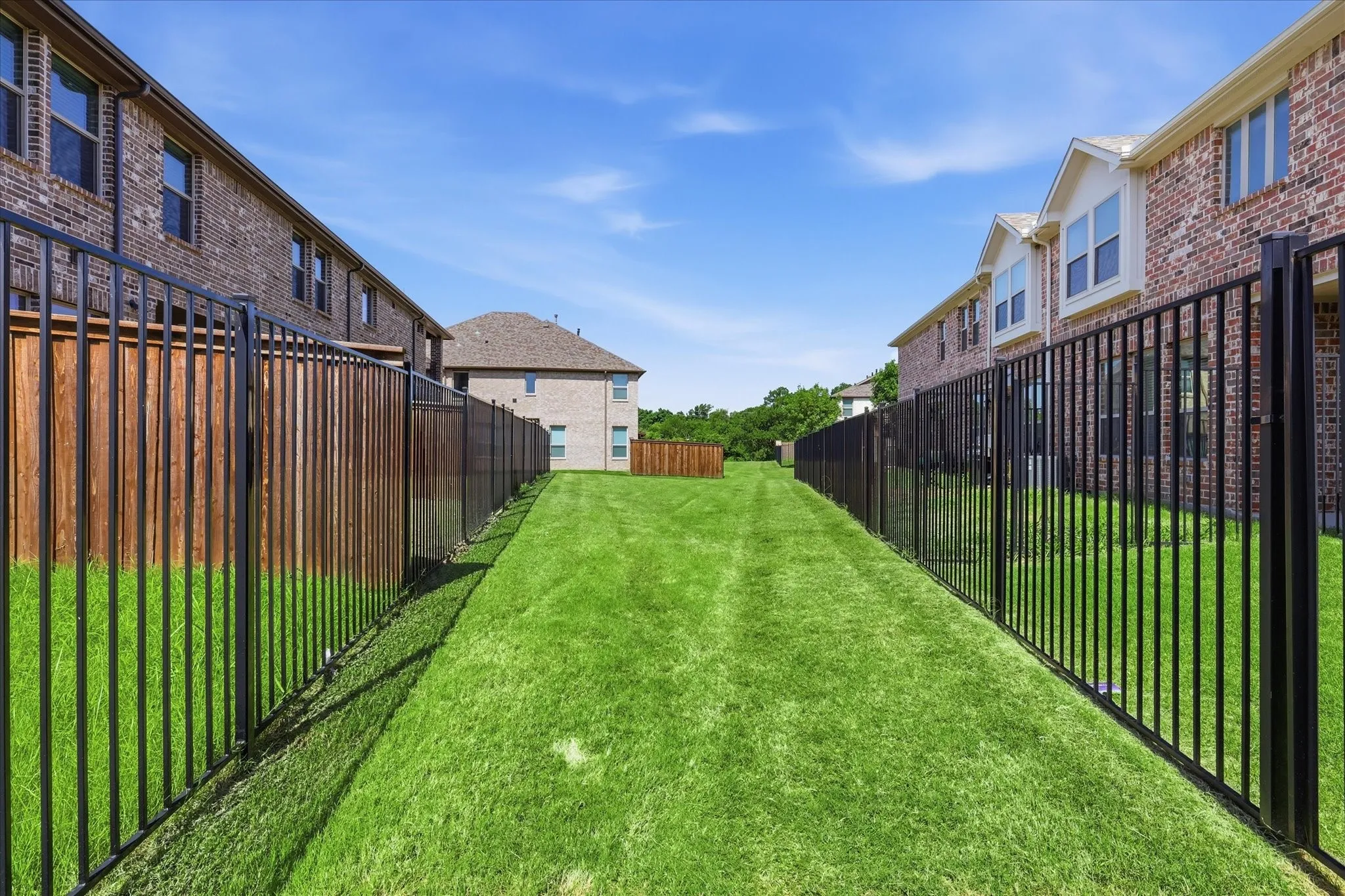 Expansive green space featuring a manicured lawn, black metal fencing, and wood privacy fencing
