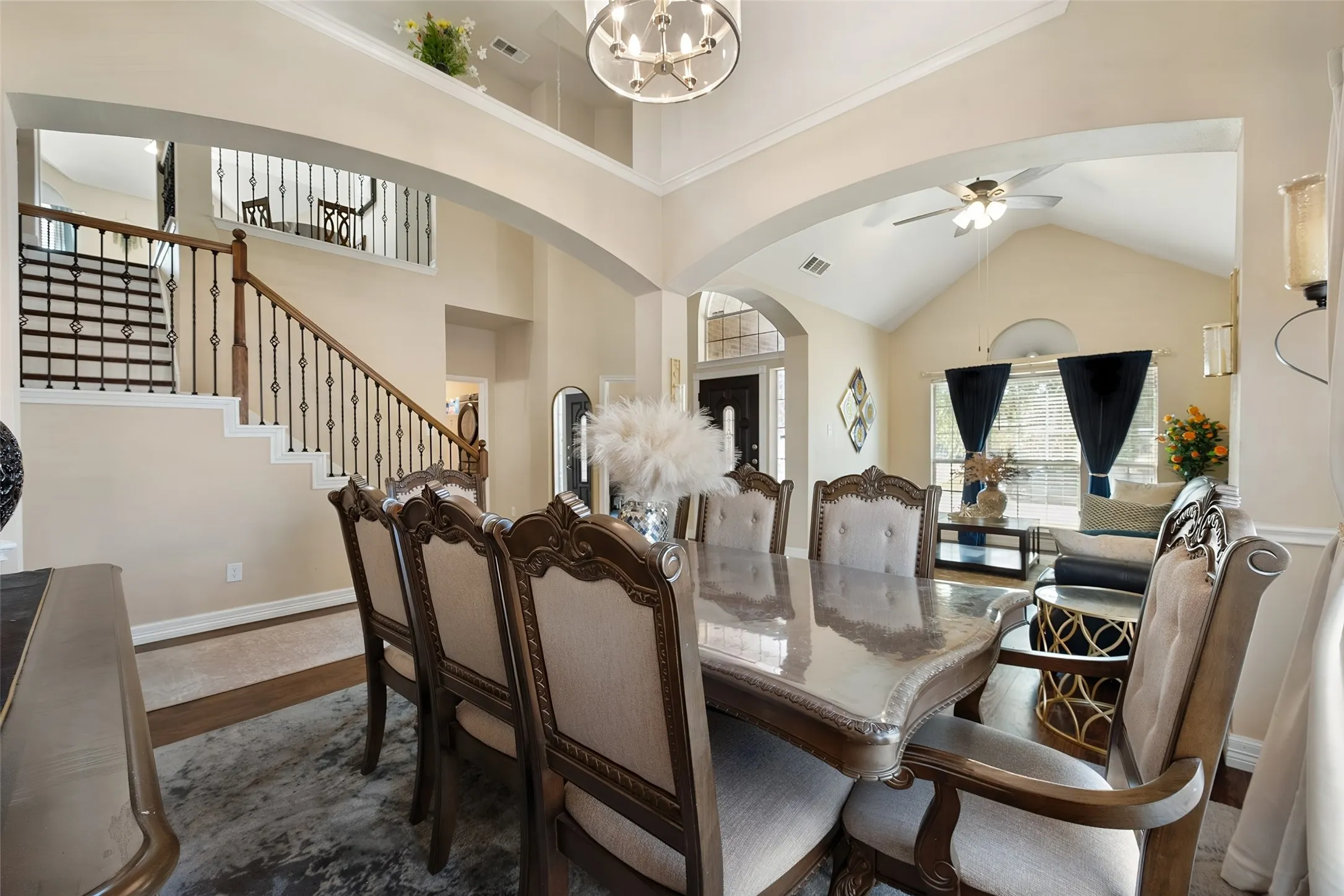 Open-concept living area with vaulted ceiling, wood-finish flooring, and a grand staircase featuring wrought iron balusters