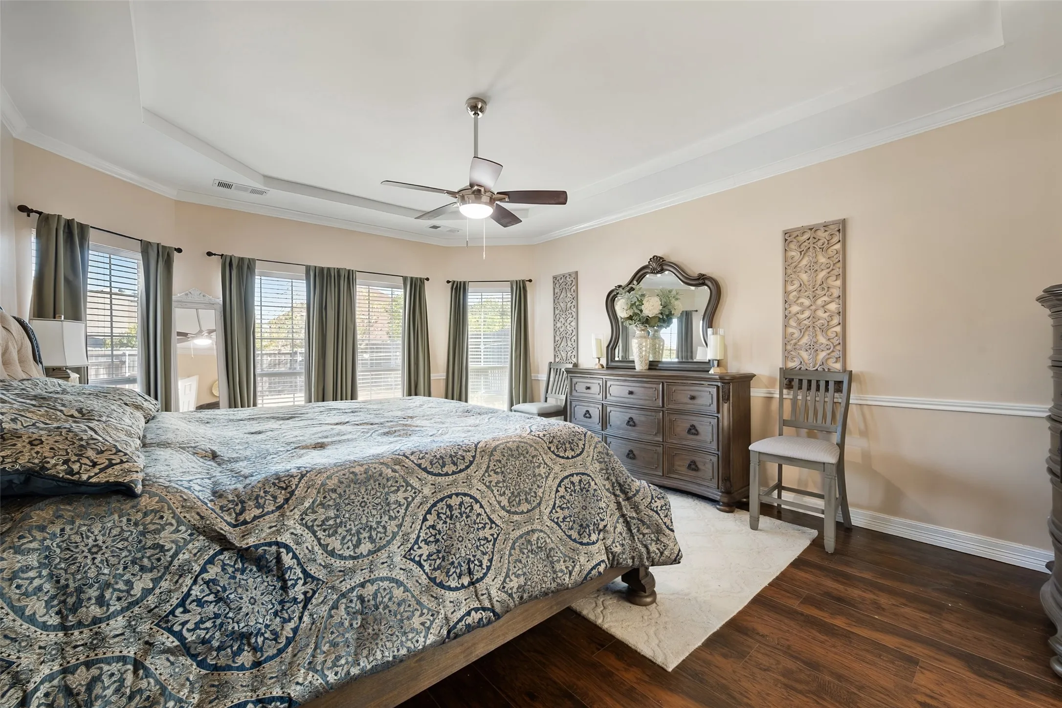 Master bedroom is downstairs,Tray ceiling, crown molding, wood-finish flooring, ceiling fan, and multiple windows with blinds