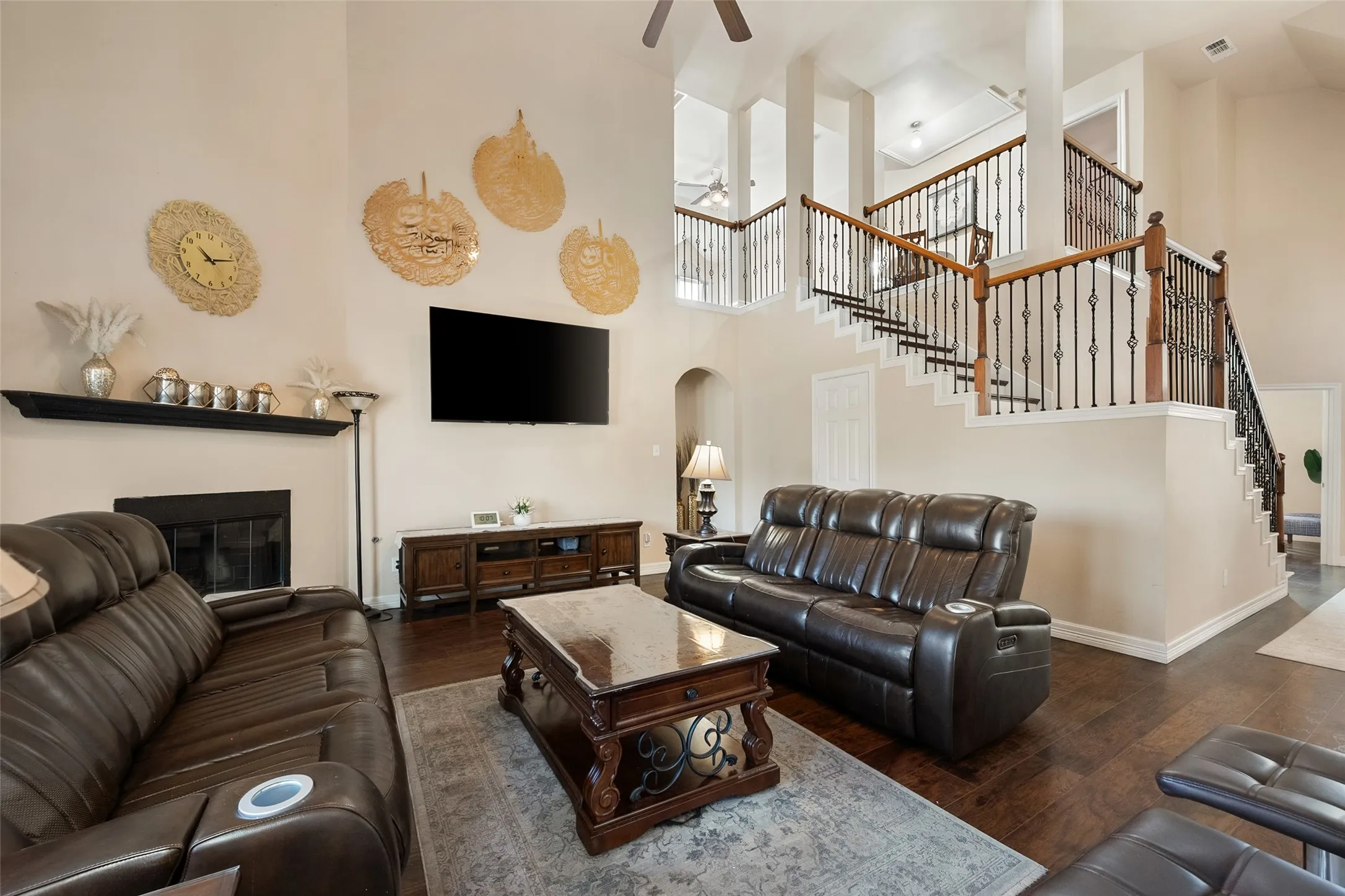  living area with high ceilings, wood-finish flooring, a fireplace with mantel, and a staircase featuring wood handrails and wrought iron balusters