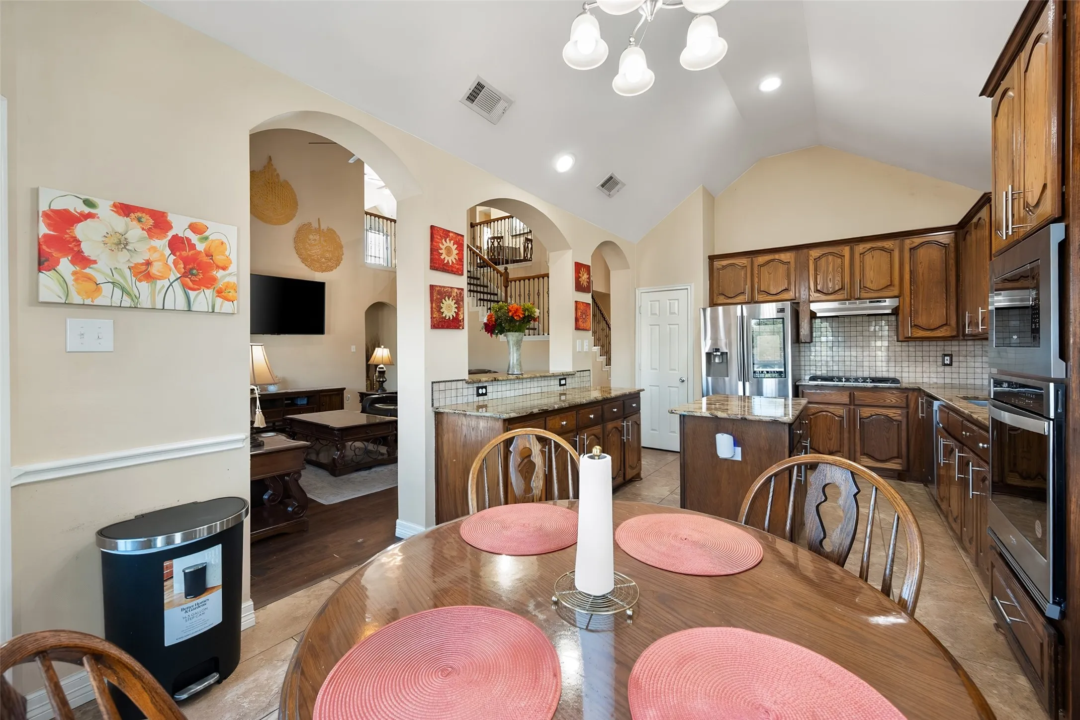 Kitchen featuring vaulted ceilings, wood cabinetry, stainless steel appliances, a center island with countertop, and tile flooring