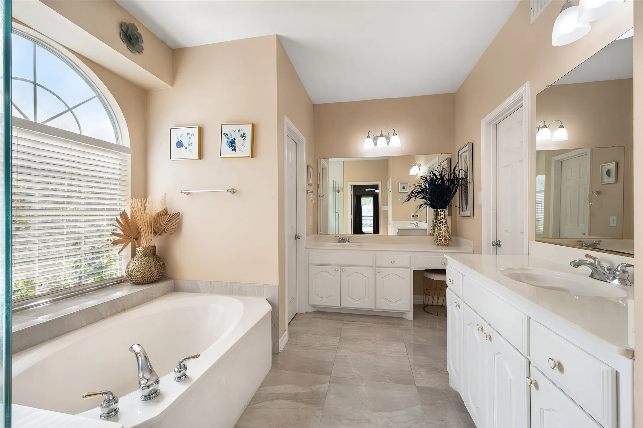 Master bathroom,Soaking tub with an arched window, dual vanity with integrated sinks, white cabinetry, and tiled flooring