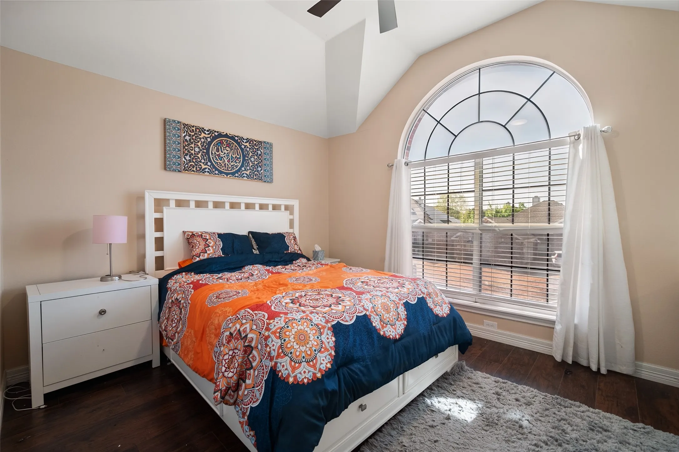 upstairs bedroom,Vaulted ceiling, arched window with gridded transom, wood-finish flooring, white window blinds, and a ceiling fan