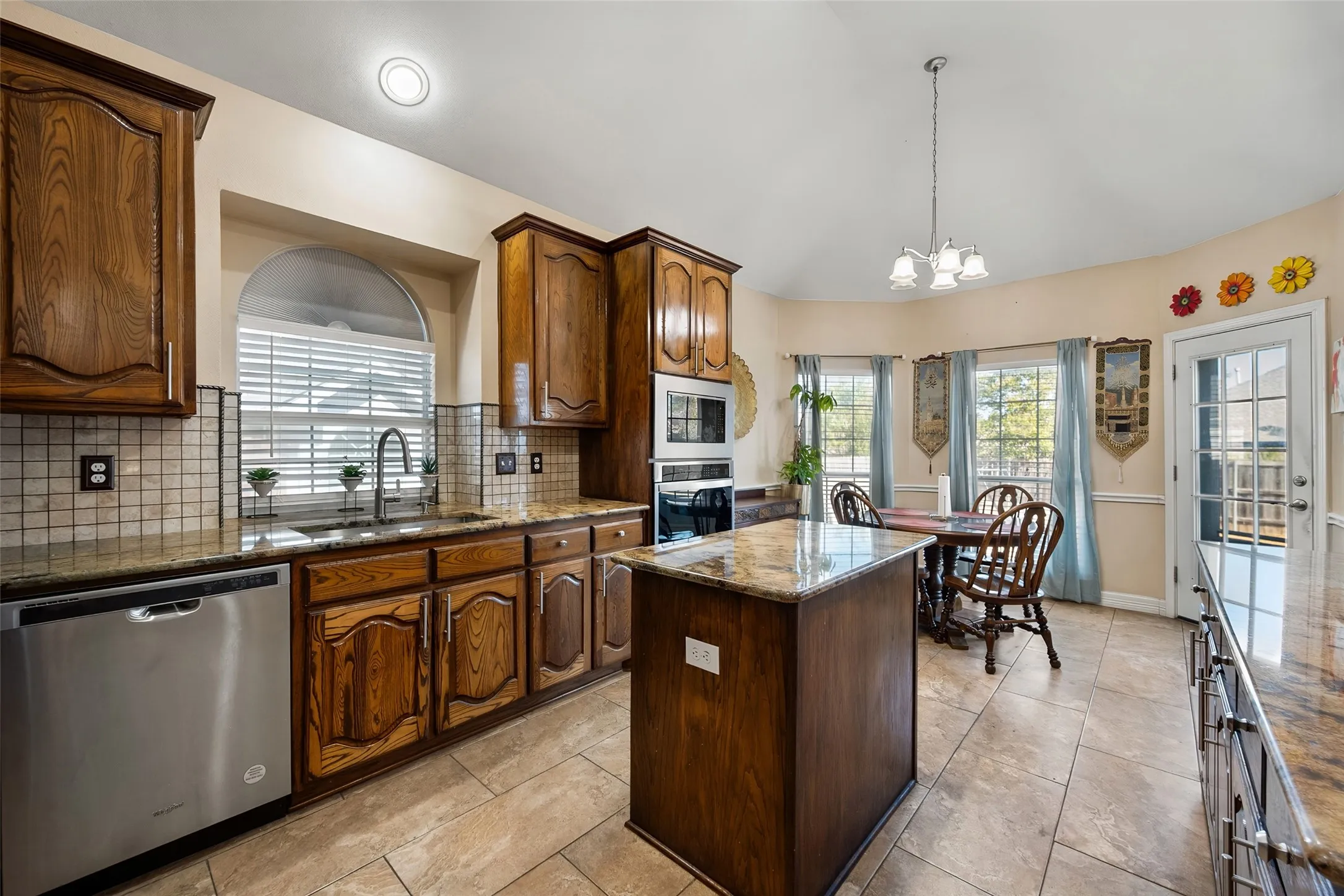 Spacious kitchen featuring wood cabinetry, stone countertops, stainless steel appliances, a center island, and tile flooring