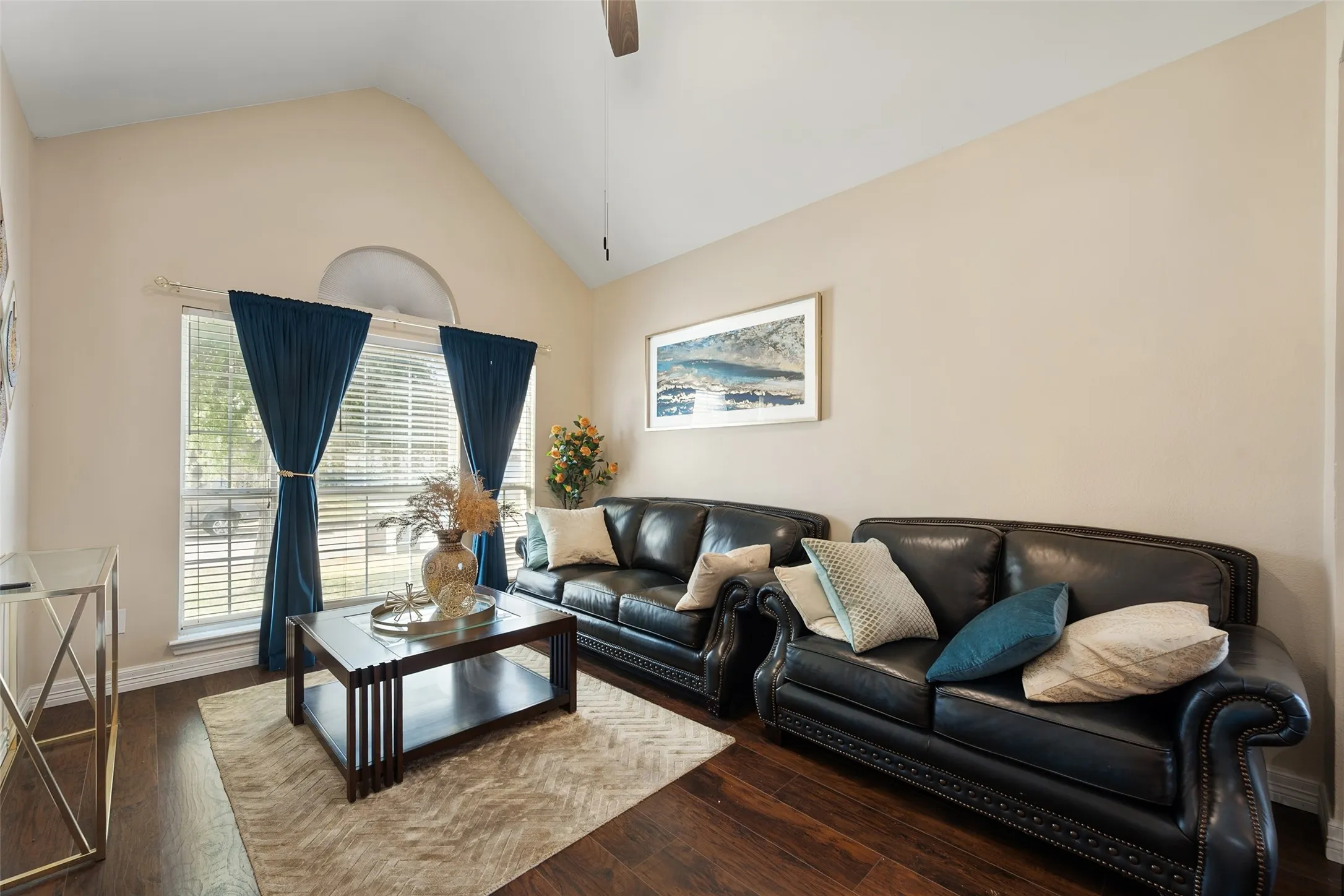 Vaulted ceiling, wood-finish flooring, large window with arched transom, neutral paint palette, and ceiling fan