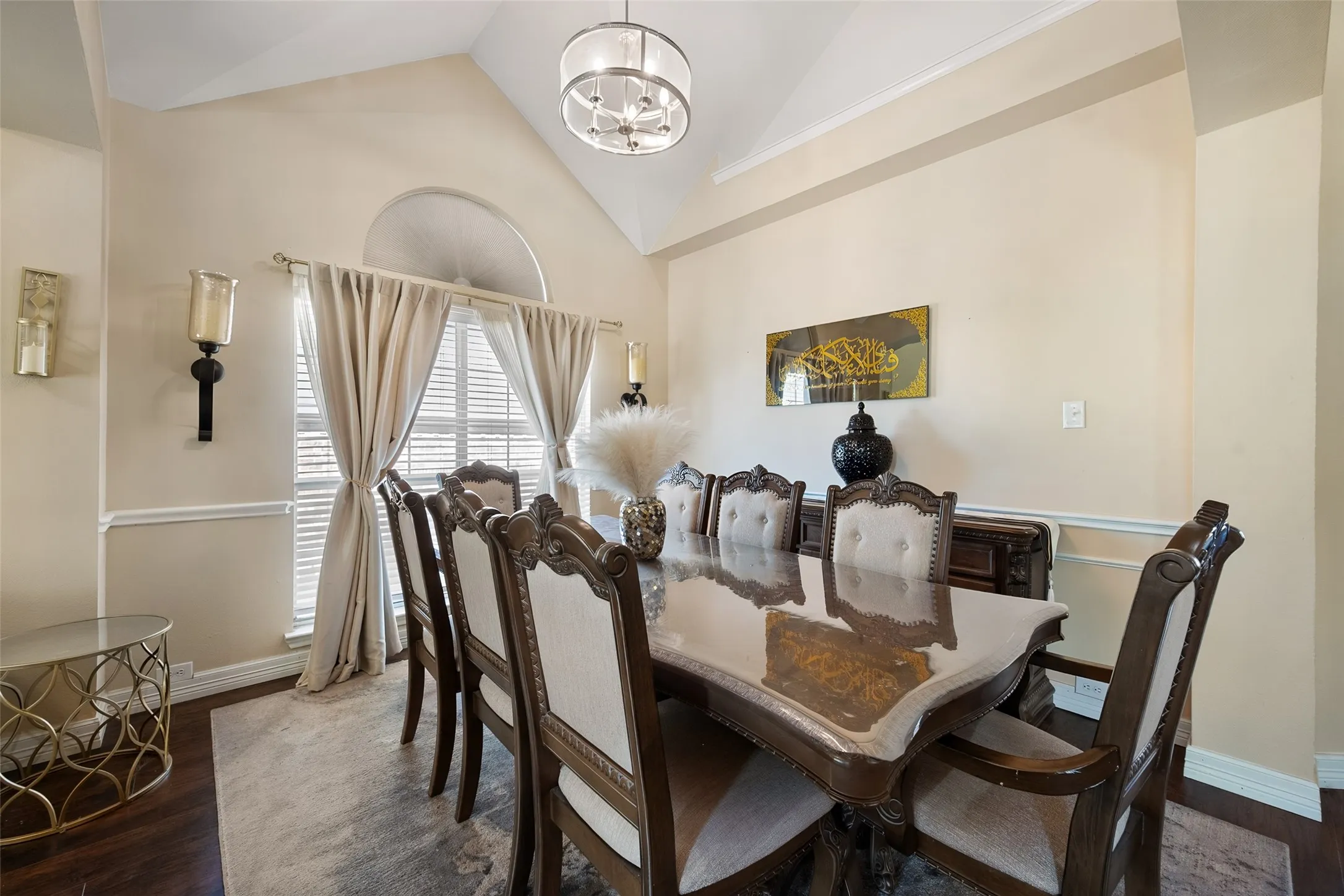Vaulted ceiling, hardwood flooring, large arched window, decorative wall sconces, and crown molding