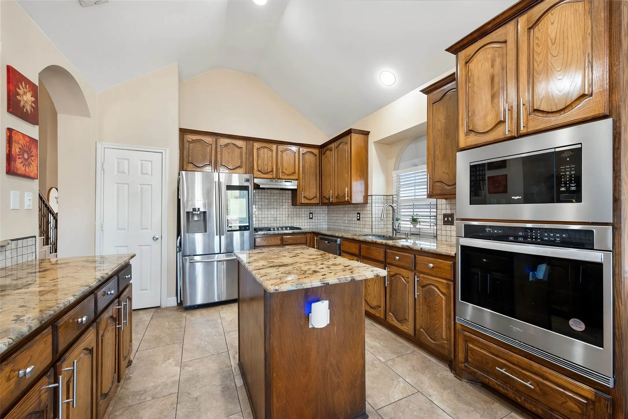 Kitchen featuring wood cabinetry, stainless steel appliances, granite countertops, and tile flooring
