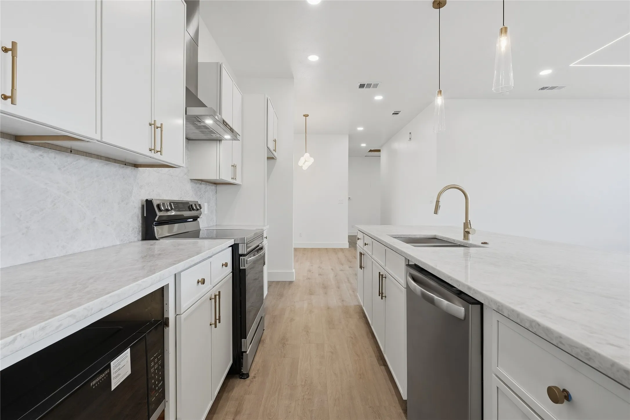 Kitchen featuring light wood-finish flooring, white cabinetry with gold-tone hardware, and light-toned countertops