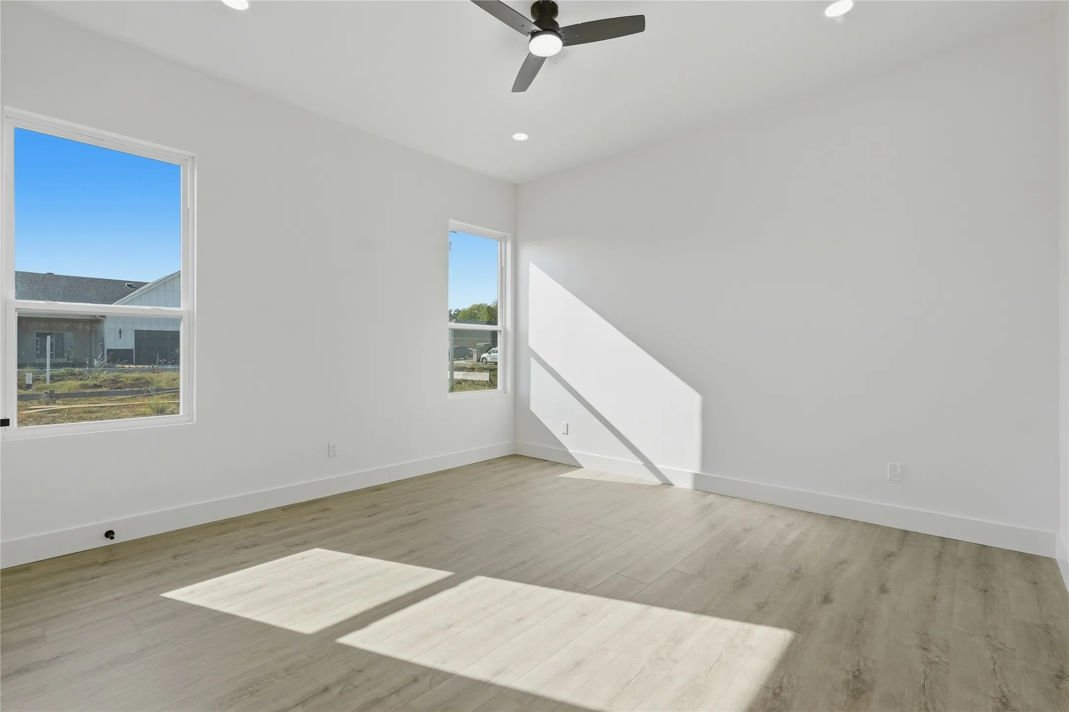 Expansive room featuring two windows, light wood-finish flooring, a ceiling fan, and recessed lighting