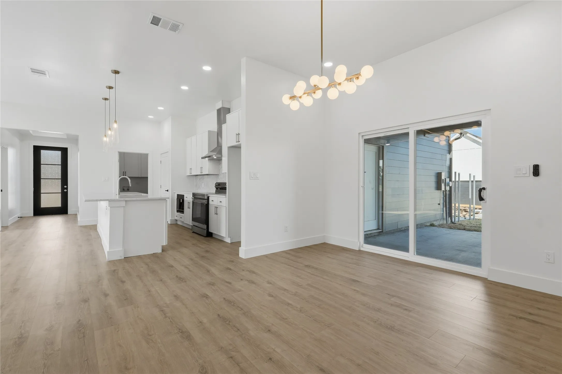Open-concept living area featuring wood-finish flooring, white cabinetry, a kitchen island with pendant lighting, stainless steel appliances, and a sliding glass door to the exterior