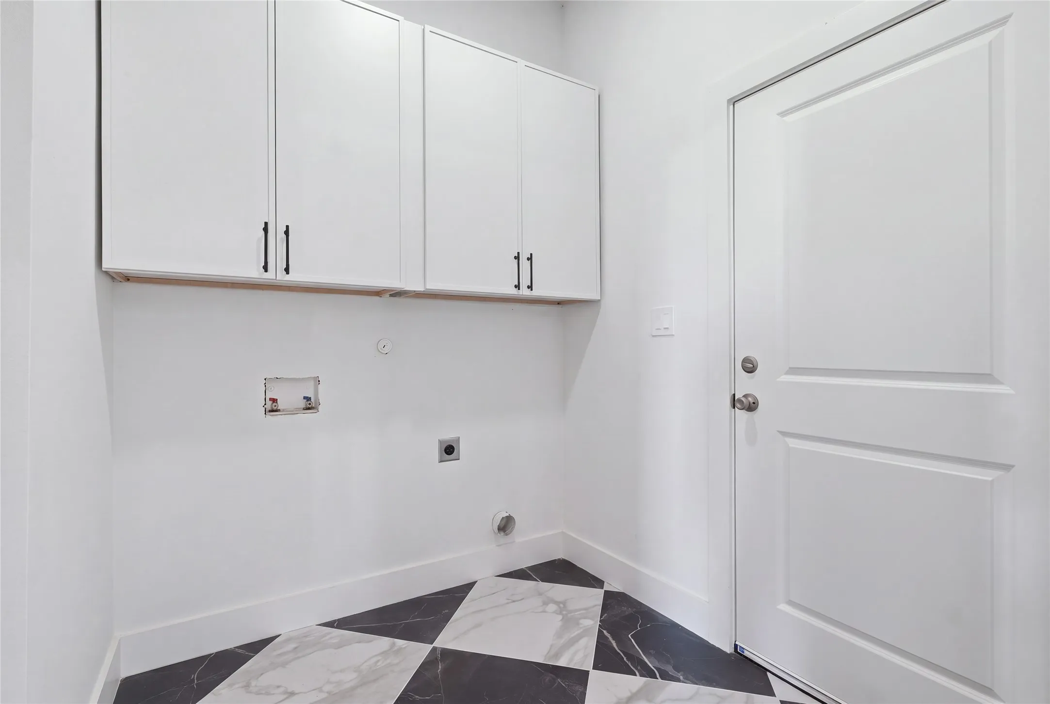 White cabinetry with black hardware, checkered floor tiling, utility hookups, and a paneled door
