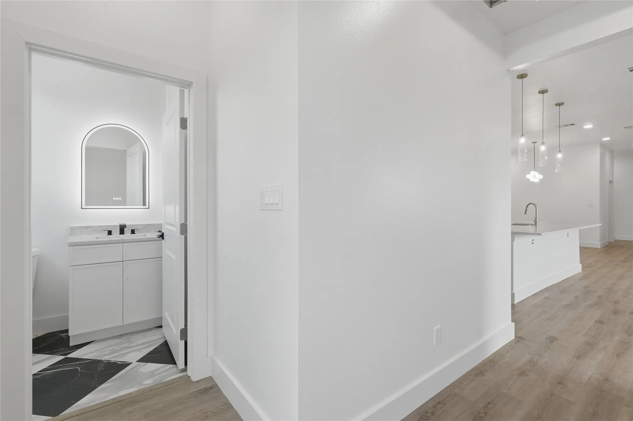 Wood-finish flooring, white walls, and a contemporary vanity with an arched illuminated mirror