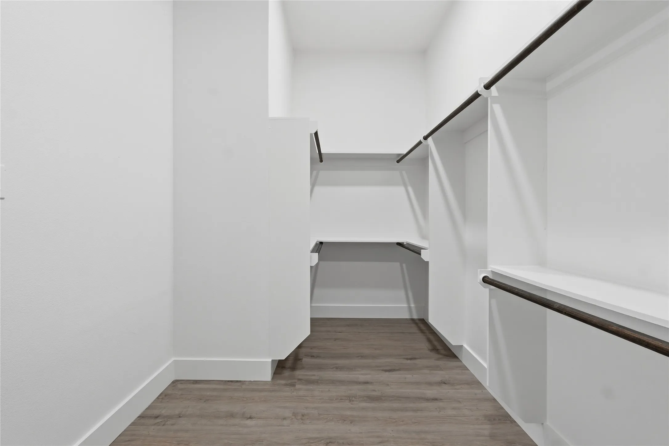 Walk-in closet with built-in shelving, hanging rods, white walls, and wood-finish flooring
