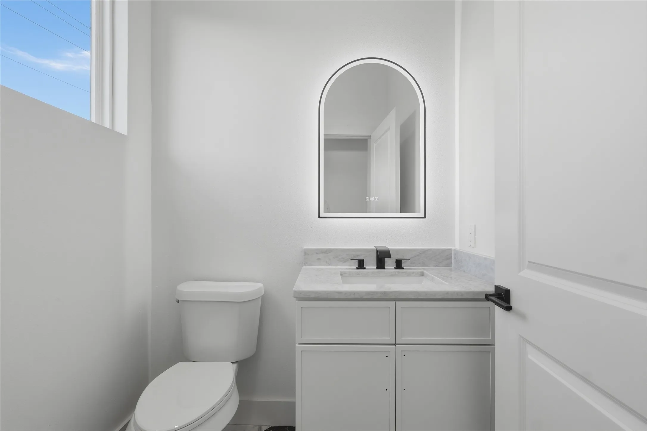 Modern bathroom featuring a white vanity with integrated sink, stone countertop, and a backlit arched mirror